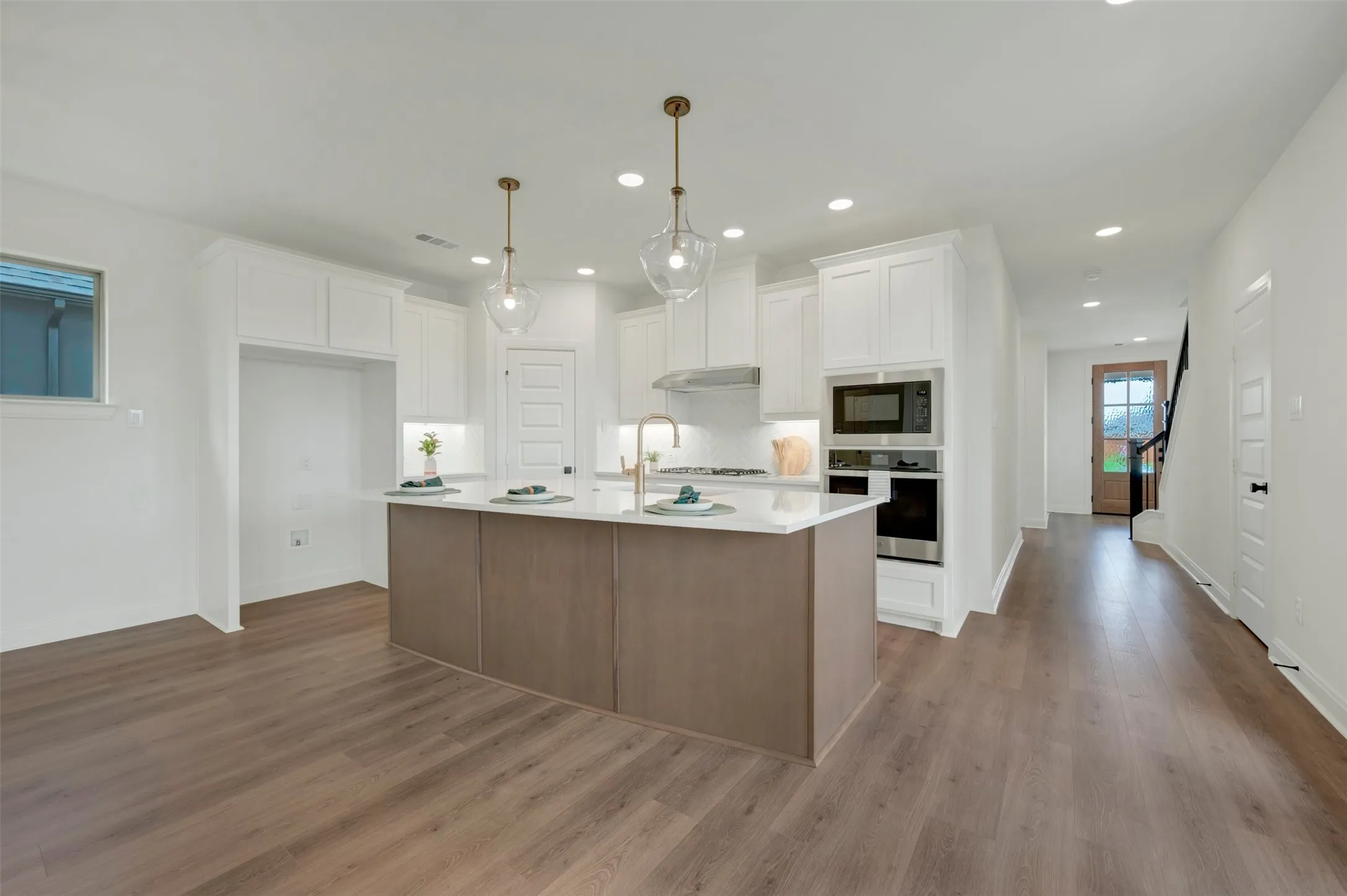 Open-concept kitchen featuring an island with seating, white shaker cabinetry, stainless steel appliances, and wood-finish flooring
