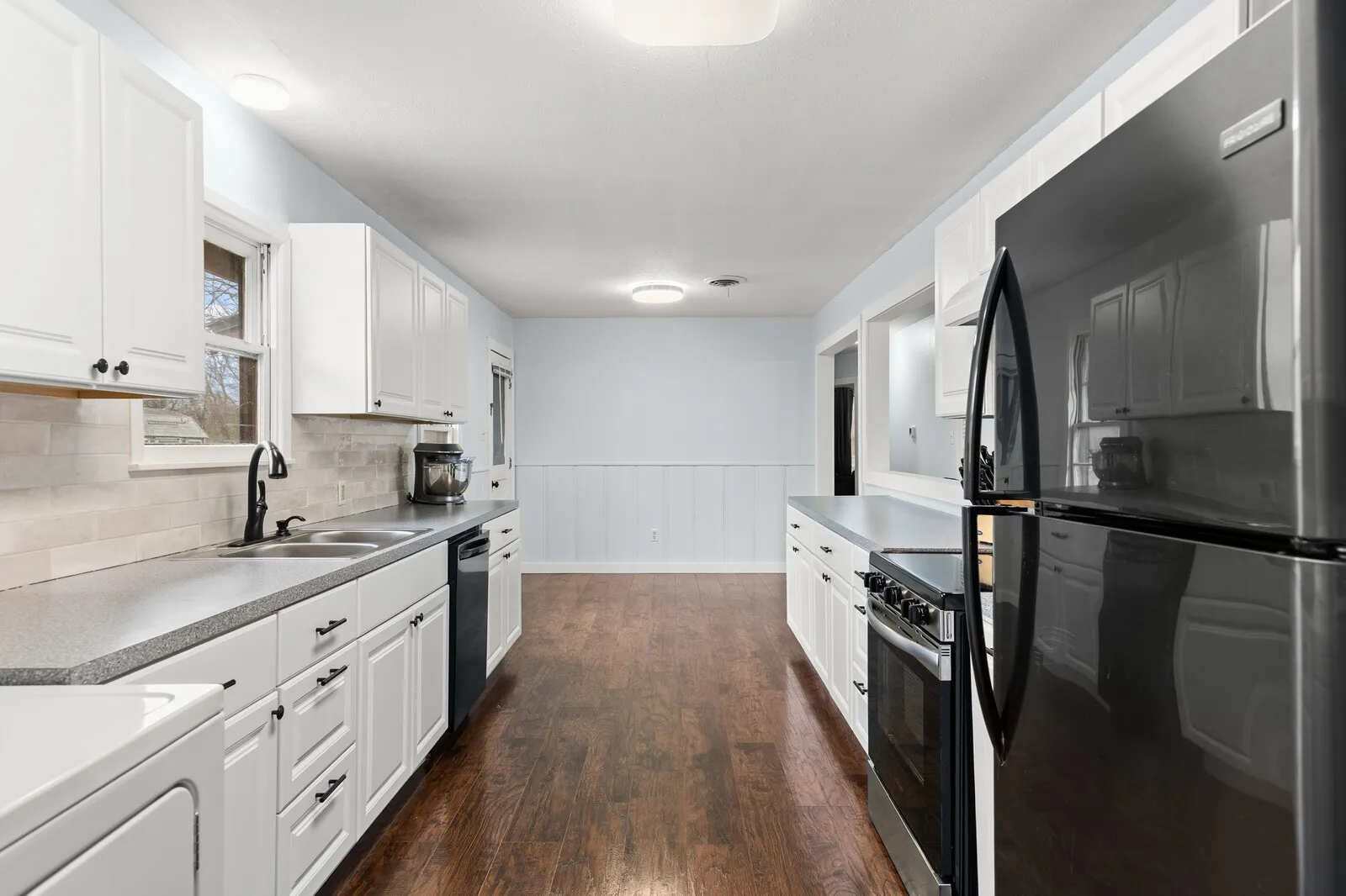 Kitchen with black appliances, white cabinets, dark wood-style flooring, wainscoting, and light countertops