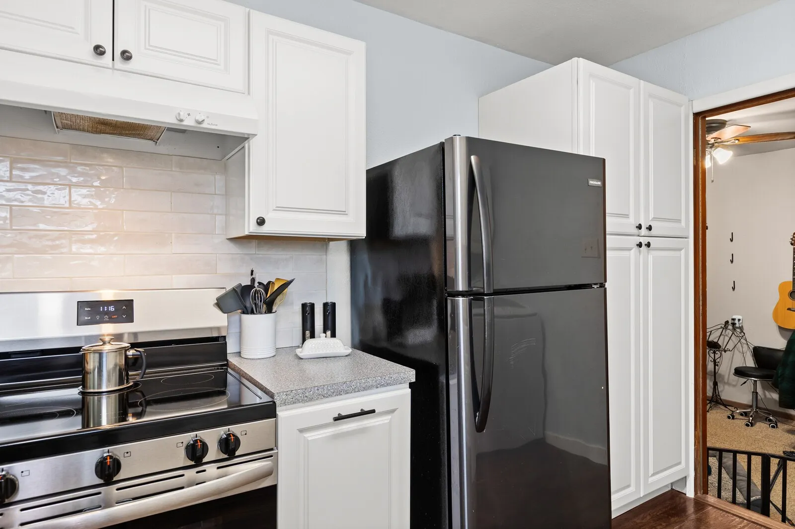 Kitchen with stainless steel electric range, freestanding refrigerator, light countertops, decorative backsplash, and under cabinet range hood