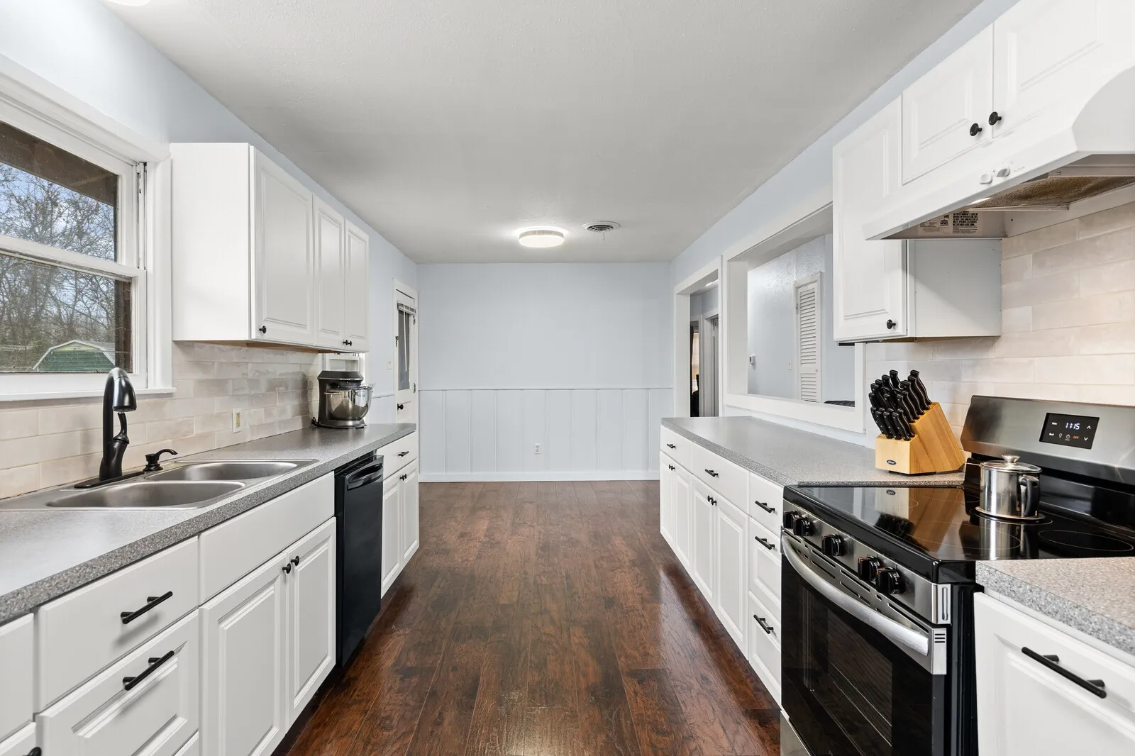 Kitchen featuring stainless steel range with electric stovetop, decorative backsplash, a wainscoted wall, white cabinets, and under cabinet range hood