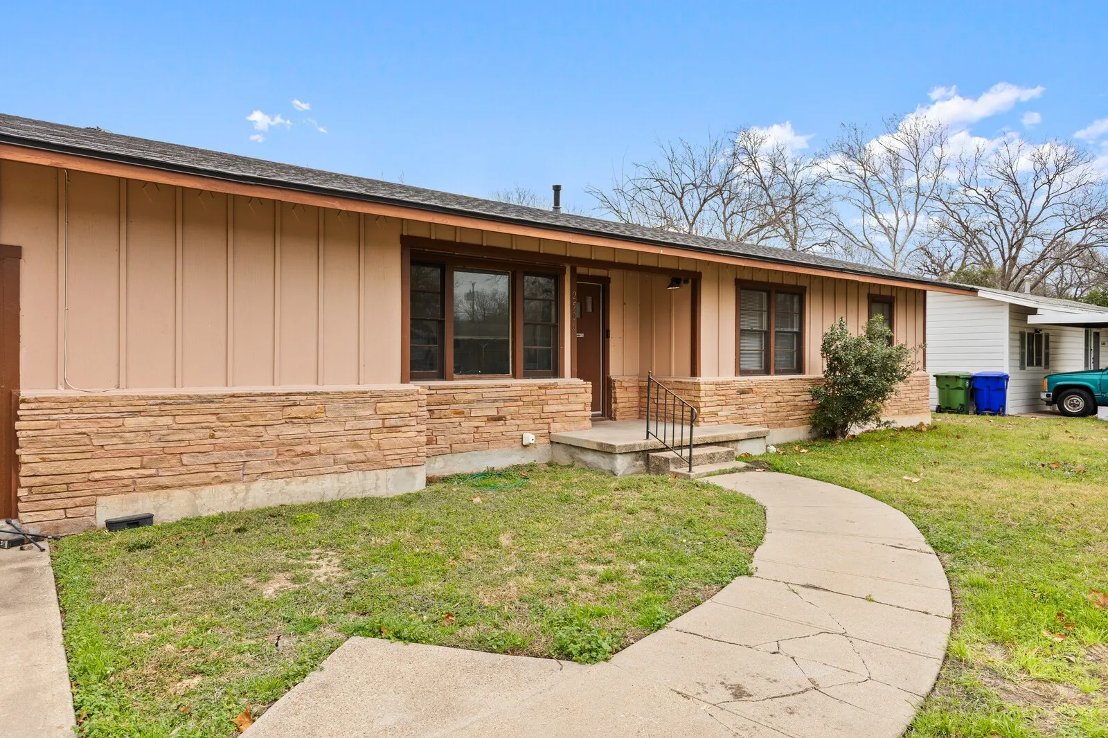 View of front of property featuring board and batten siding, a front lawn, stone siding, covered porch, and a shingled roof