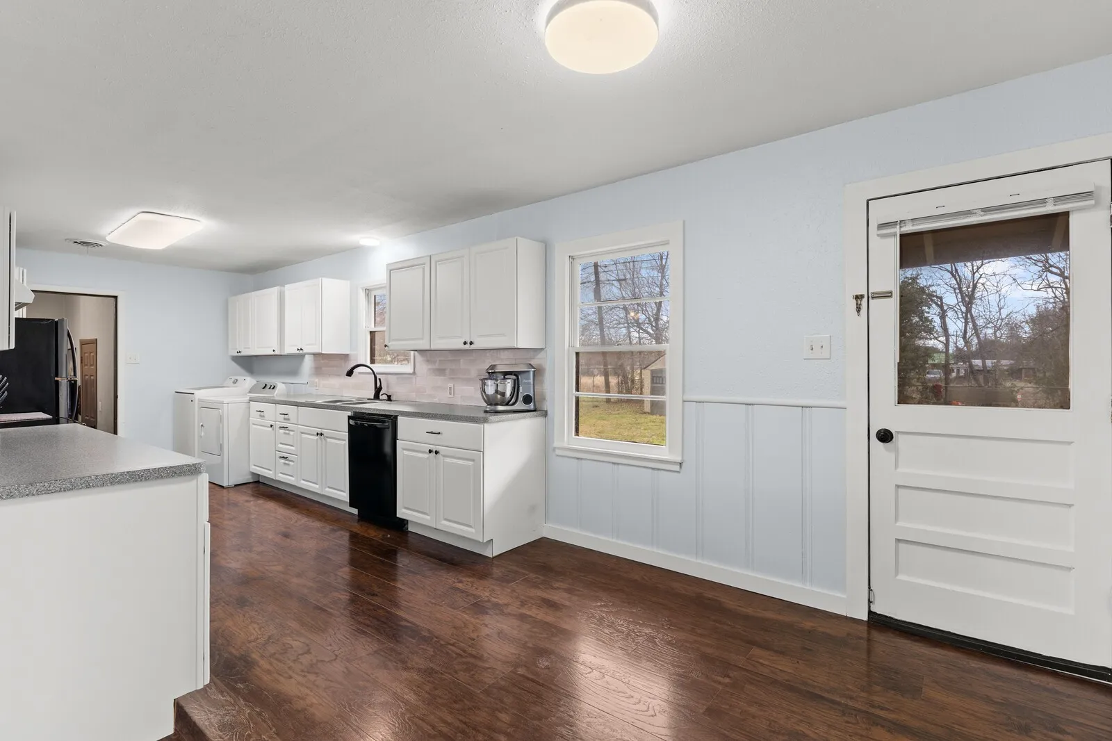 Kitchen featuring a wainscoted wall, dark wood-style floors, white cabinets, freestanding refrigerator, and dishwasher