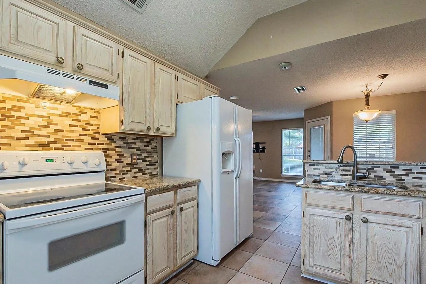 Kitchen featuring white appliances, tasteful backsplash, lofted ceiling, pendant lighting, and under cabinet range hood