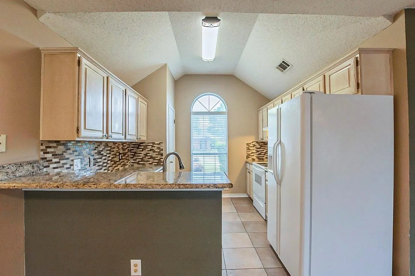 Kitchen with white appliances, backsplash, a peninsula, light stone countertops, and light tile patterned floors