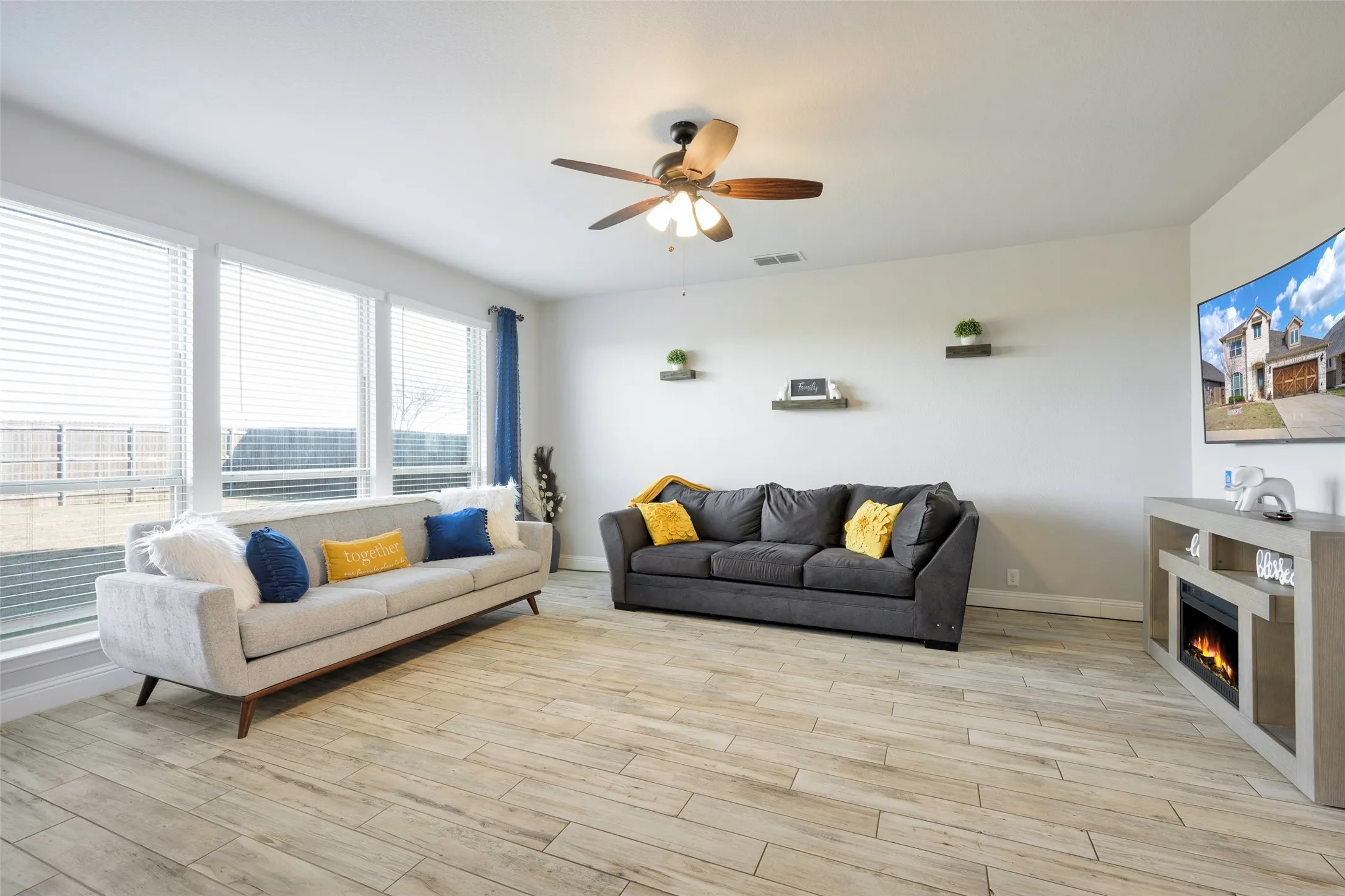 Living area with a ceiling fan, light wood-style flooring, and a warm lit fireplace