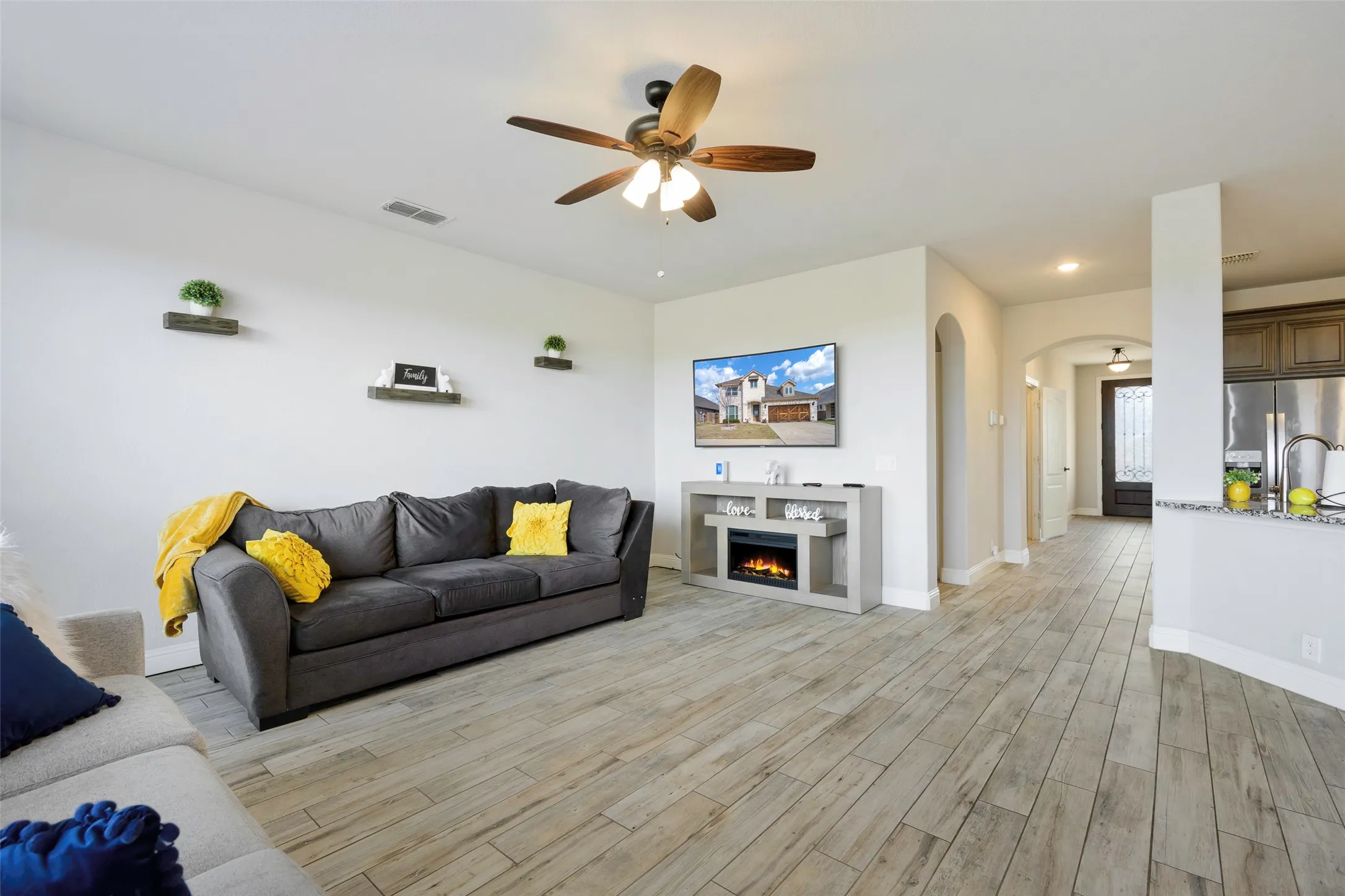 Living room featuring a warm lit fireplace, ceiling fan, arched walkways, light wood-type flooring, and recessed lighting