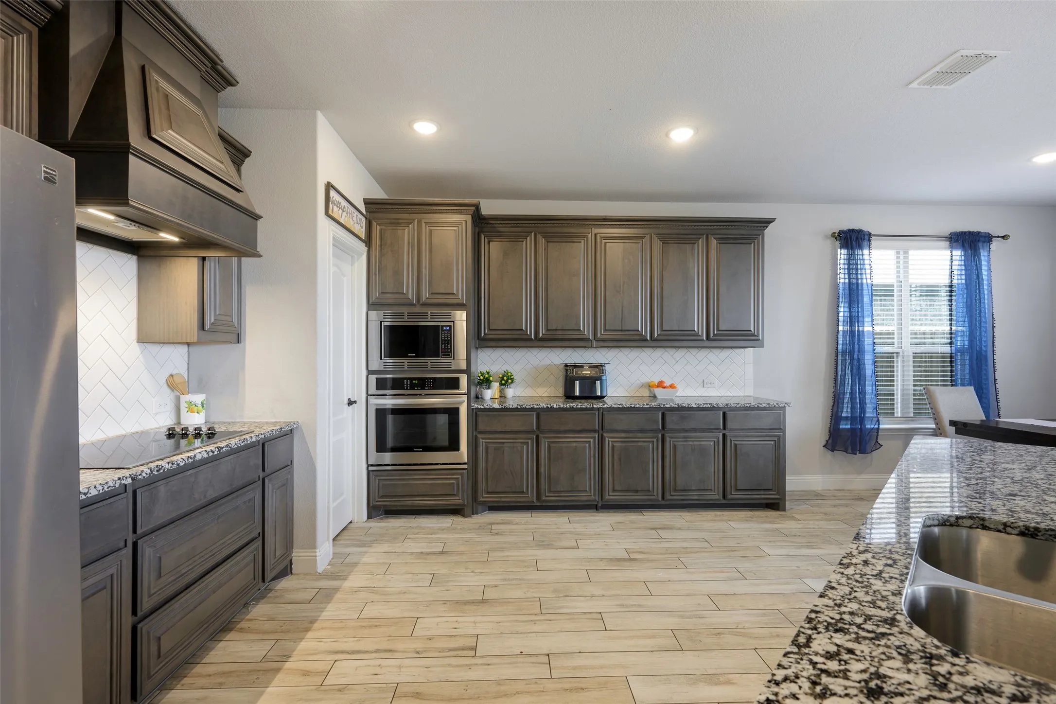 Kitchen with dark brown cabinets, premium range hood, stainless steel appliances, light stone countertops, and recessed lighting