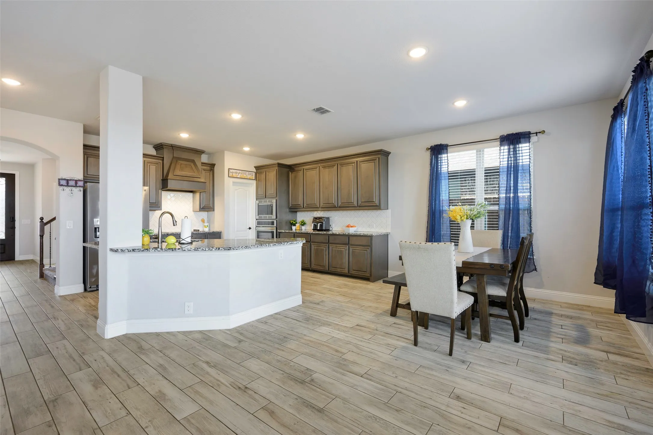Kitchen with light stone countertops, arched walkways, stainless steel appliances, custom range hood, and light wood-type flooring