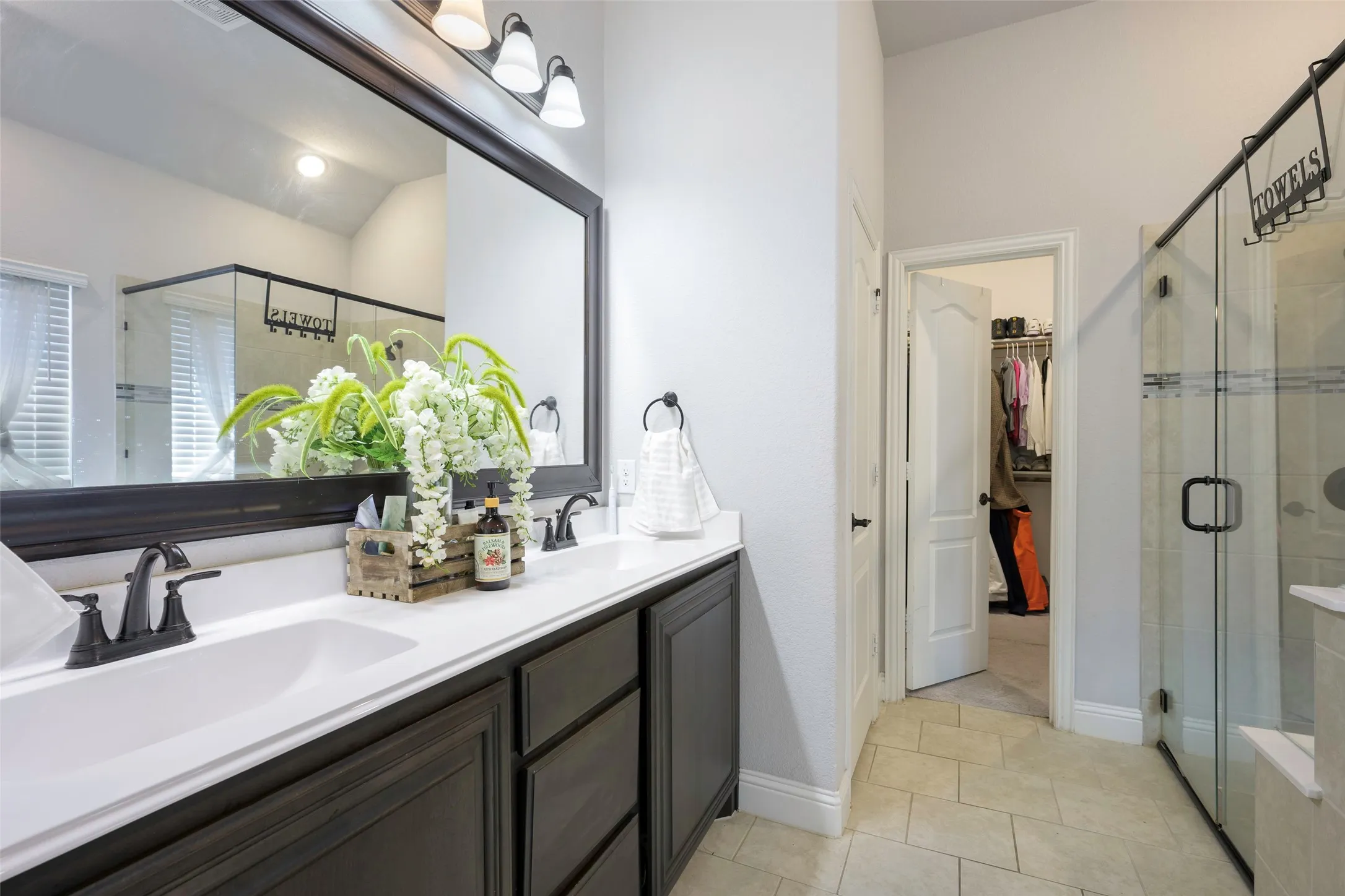 Primary Bathroom featuring a stall shower, double vanity, a walk in closet, and light tile patterned floors