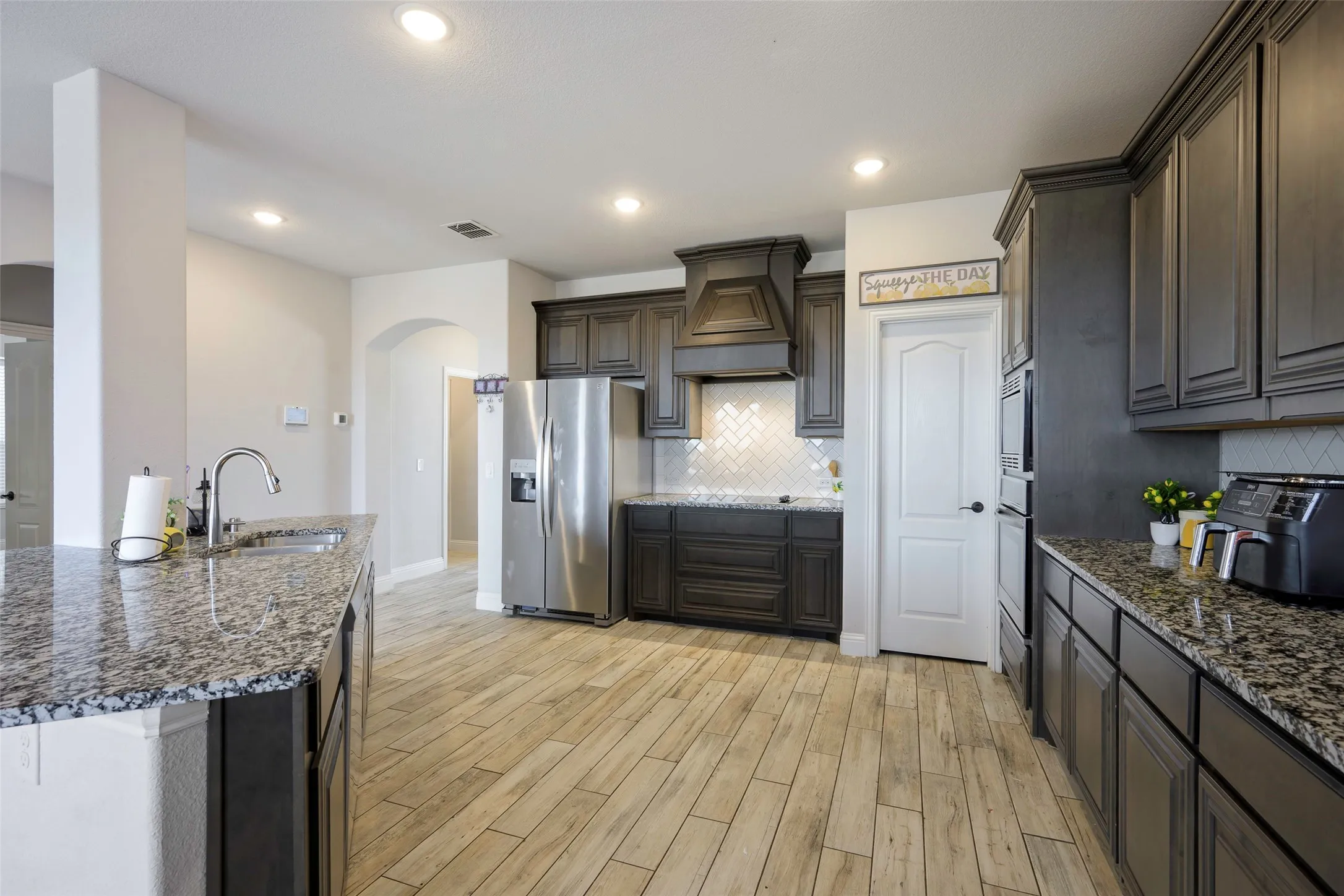 Kitchen featuring dark stone counters, stainless steel appliances, custom exhaust hood, arched walkways, and light wood-style floors