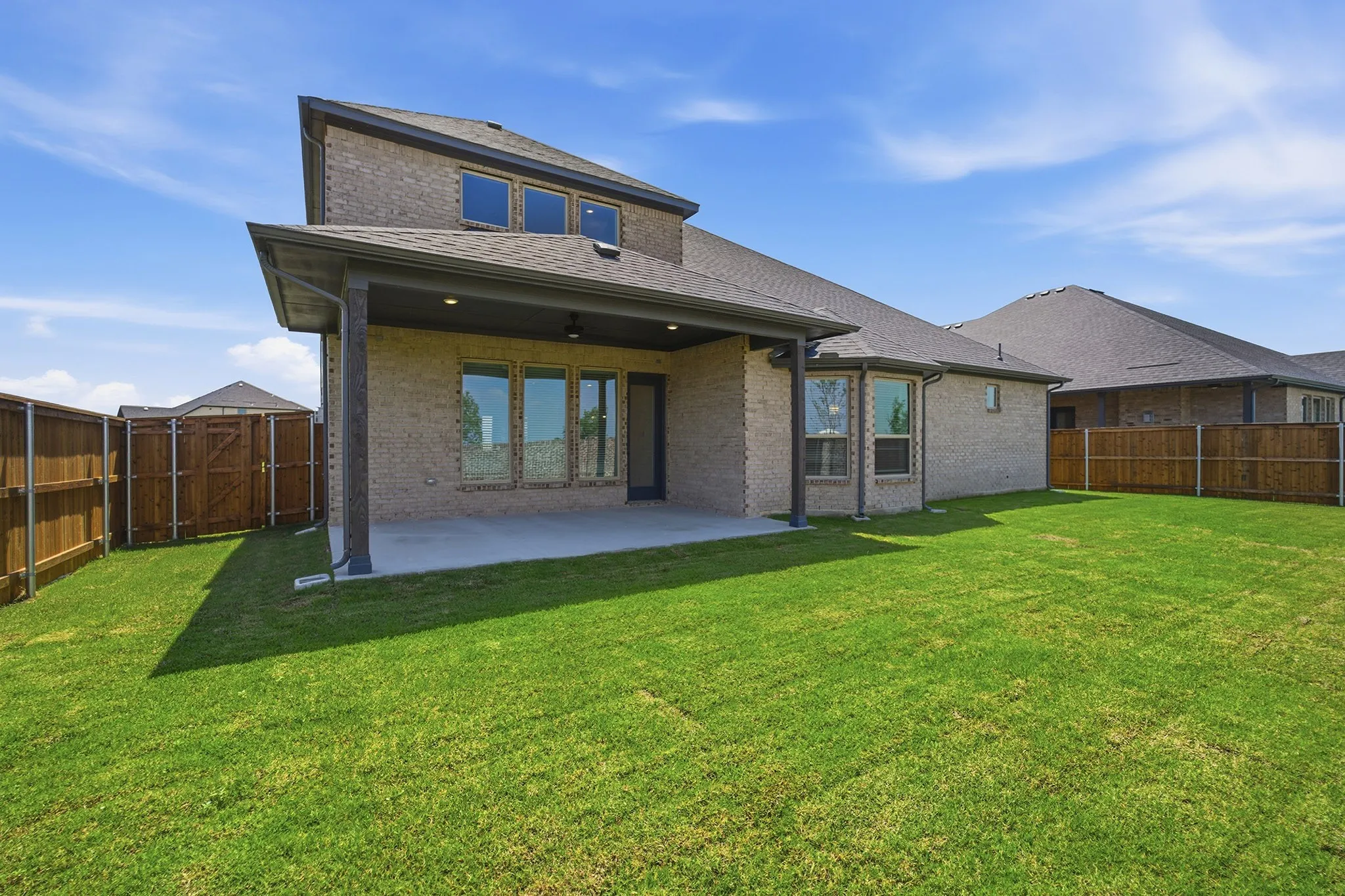 Expansive backyard featuring a manicured lawn, full privacy fencing, and a covered patio with recessed lighting