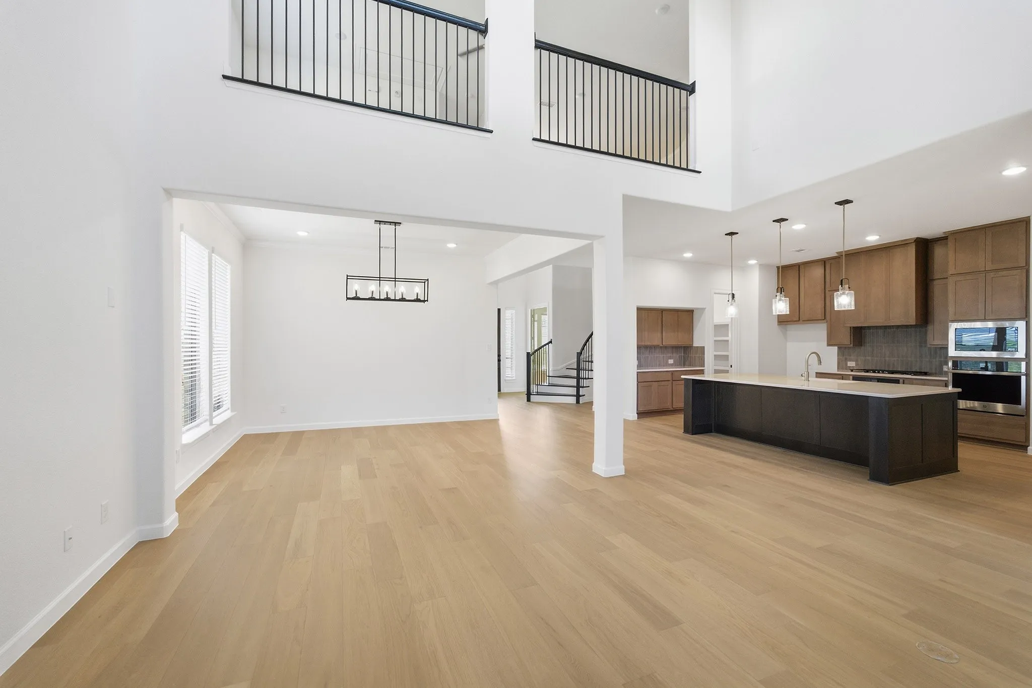 Open-concept living area with two-story ceilings, light wood-finish flooring, and crisp white walls