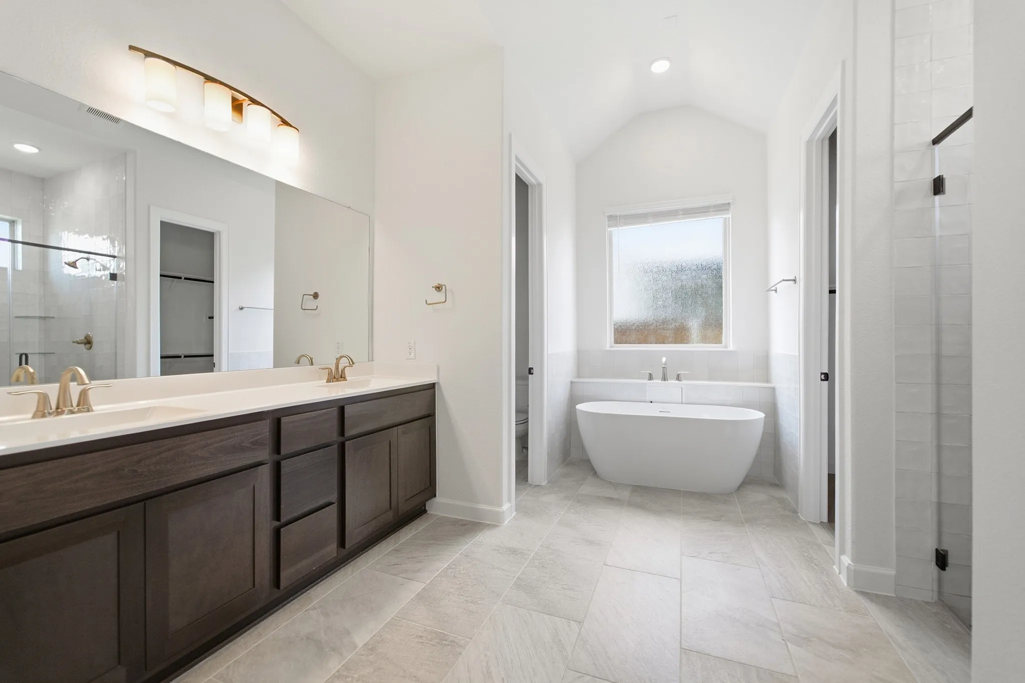 Spacious bathroom featuring a dual vanity with dark wood-finish cabinetry and white countertops, large wall-mounted mirror, freestanding soaking tub, and walk-in shower with clear glass enclosure