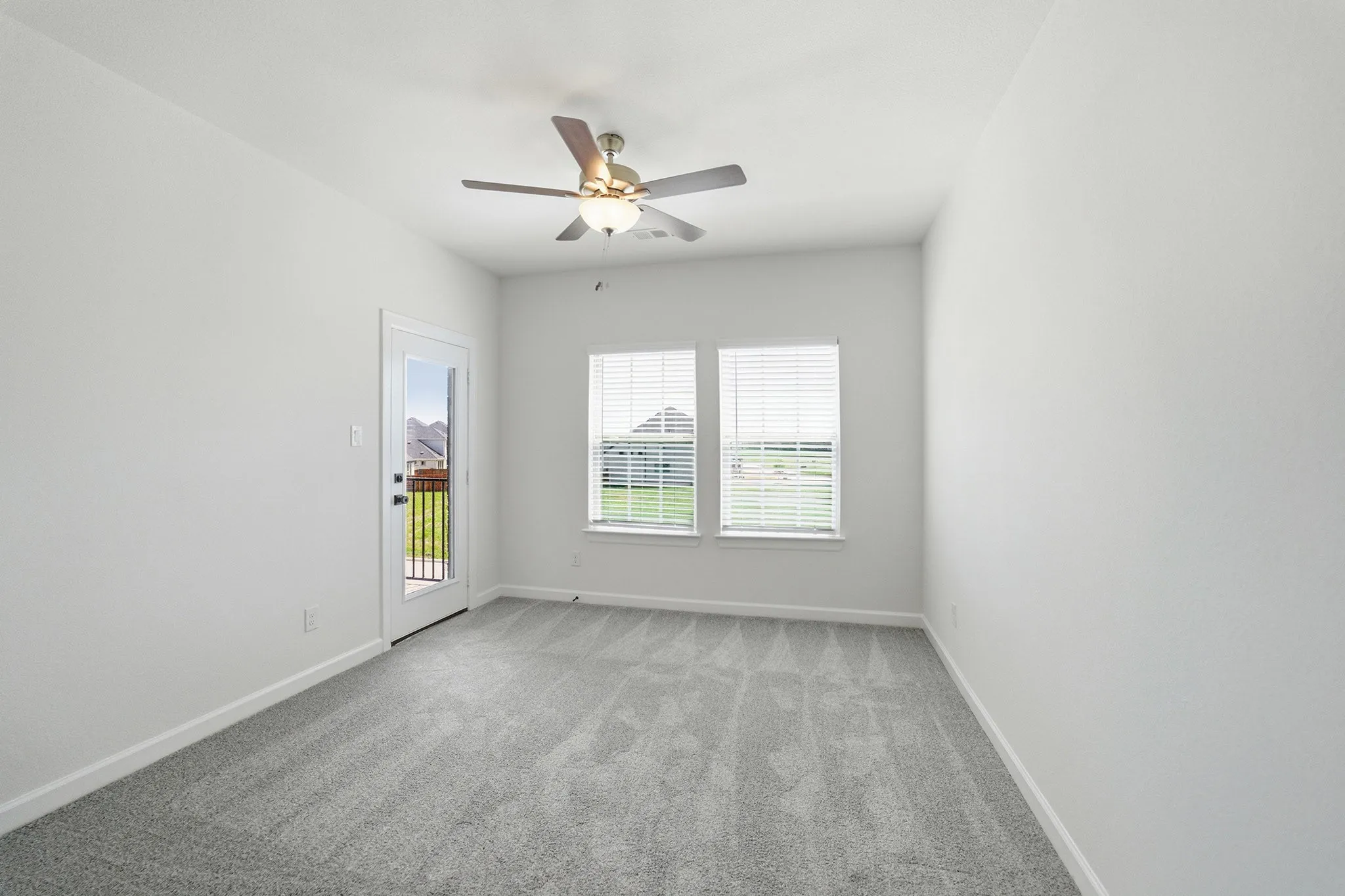 Bright room featuring light gray carpeting, a ceiling fan with integrated lighting, two windows with blinds, and a glass-paneled door