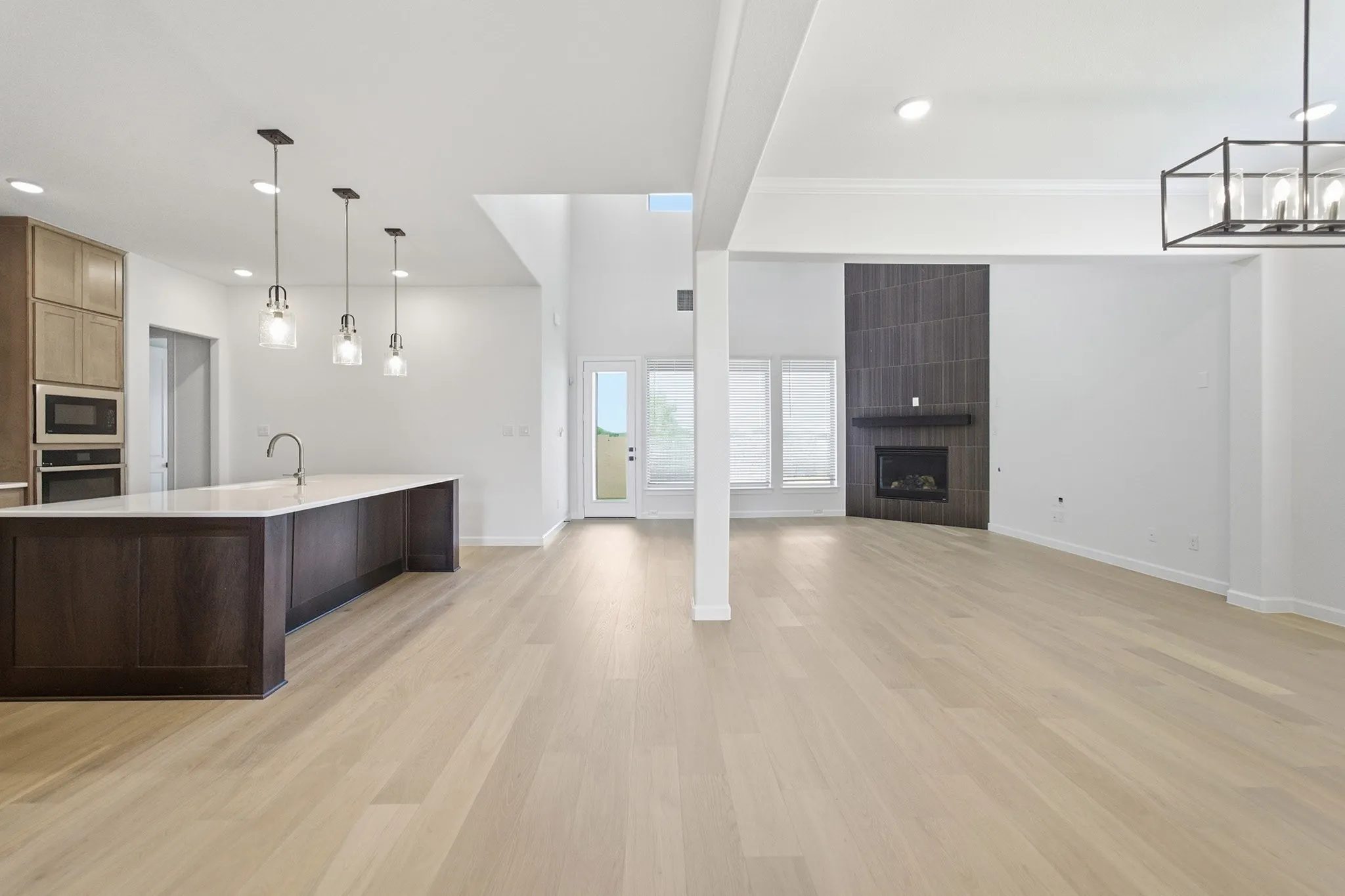Spacious interior featuring light wood-finish flooring, a kitchen island with pendant lighting, a tile-accented fireplace, numerous windows, and high ceilings