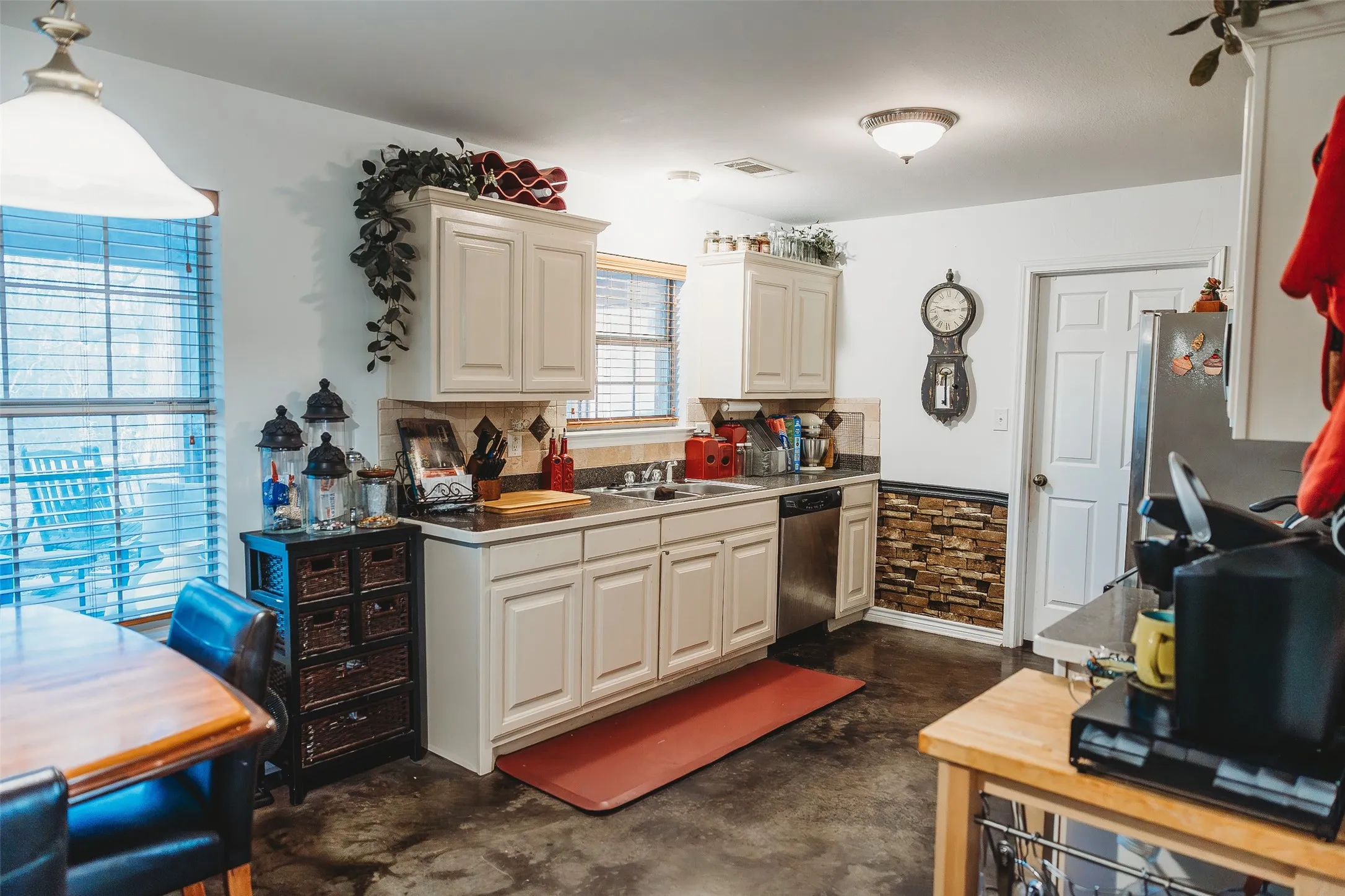 Kitchen with finished concrete flooring, stainless steel dishwasher, hanging light fixtures, tasteful backsplash, and light countertops