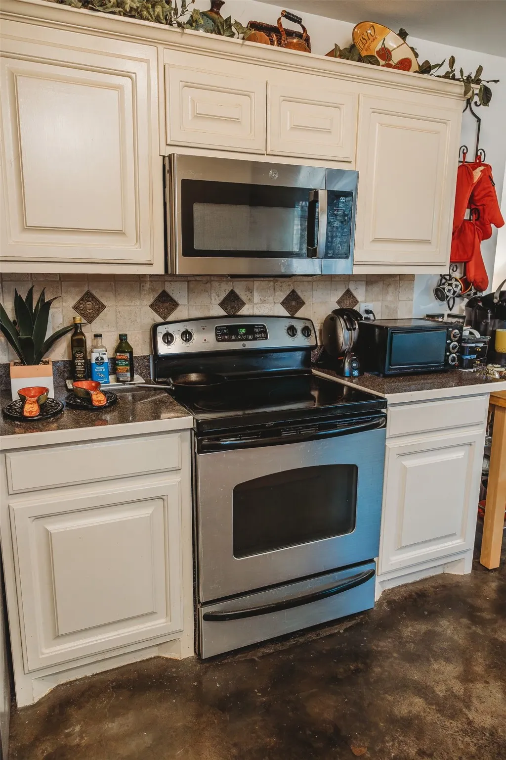 Kitchen with appliances with stainless steel finishes, dark countertops, concrete flooring, and decorative backsplash