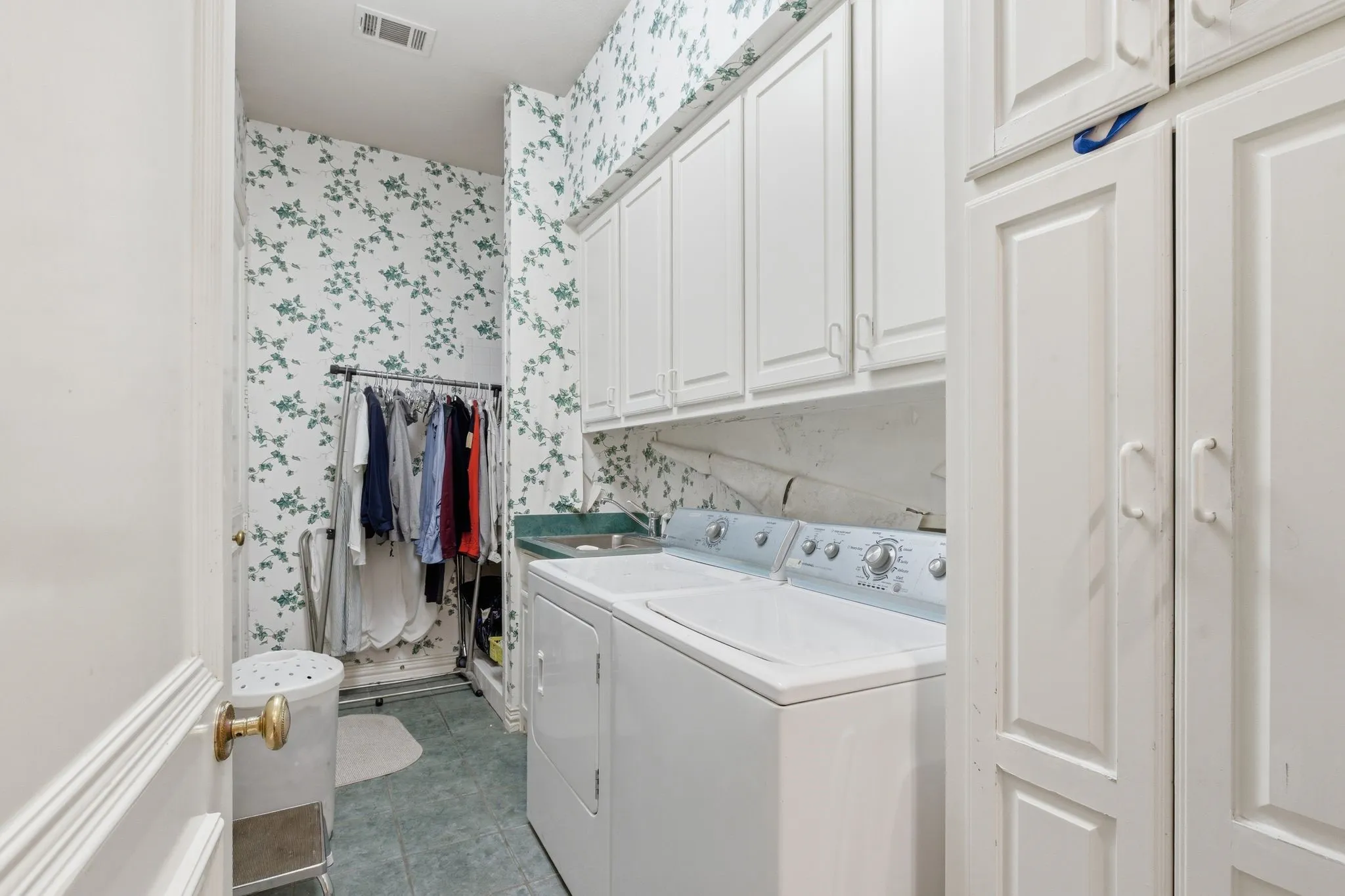 Laundry room featuring cabinet space, wallpapered walls, and separate washer and dryer