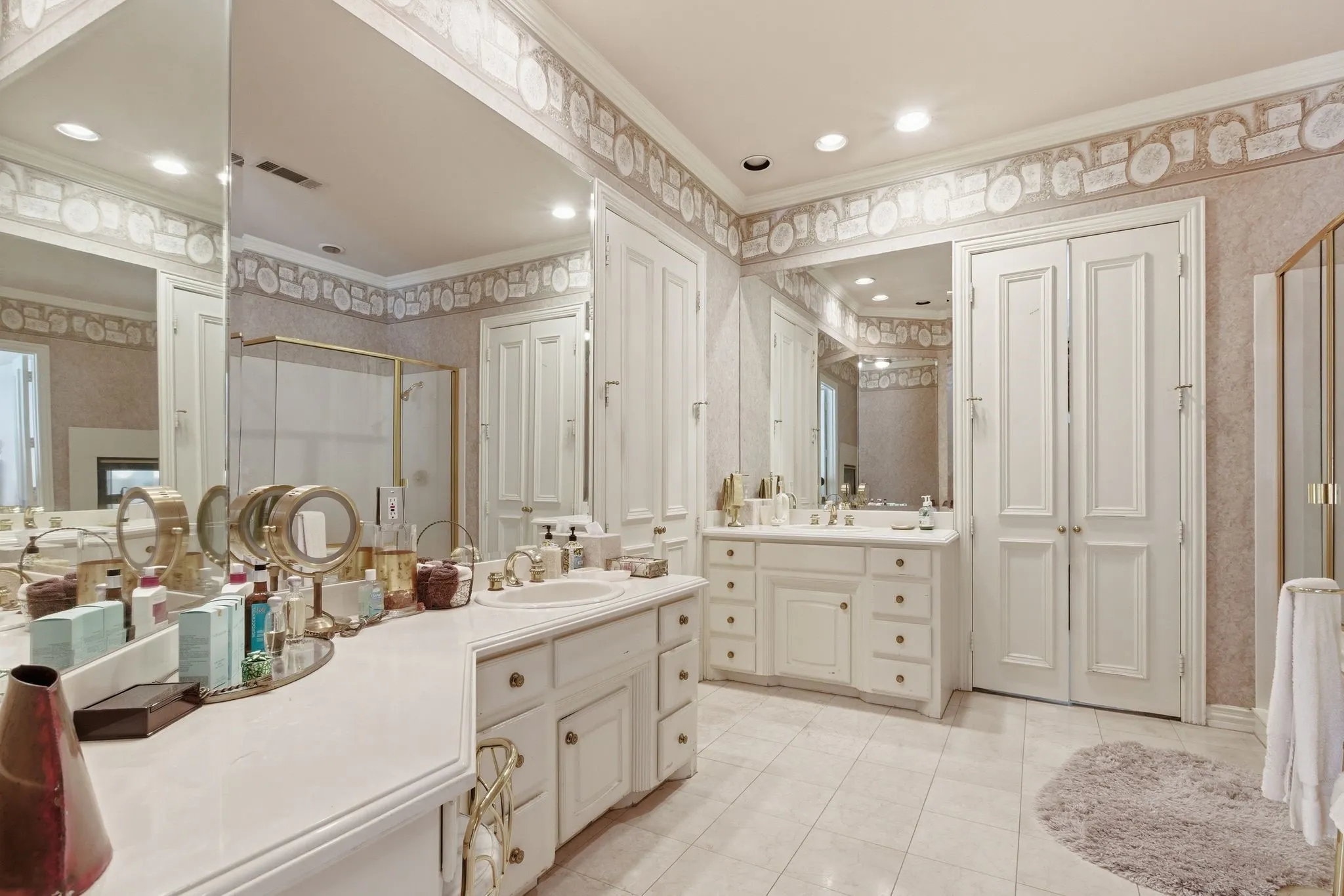 Full bathroom with crown molding, two vanities, a closet, wallpapered walls, and a stall shower