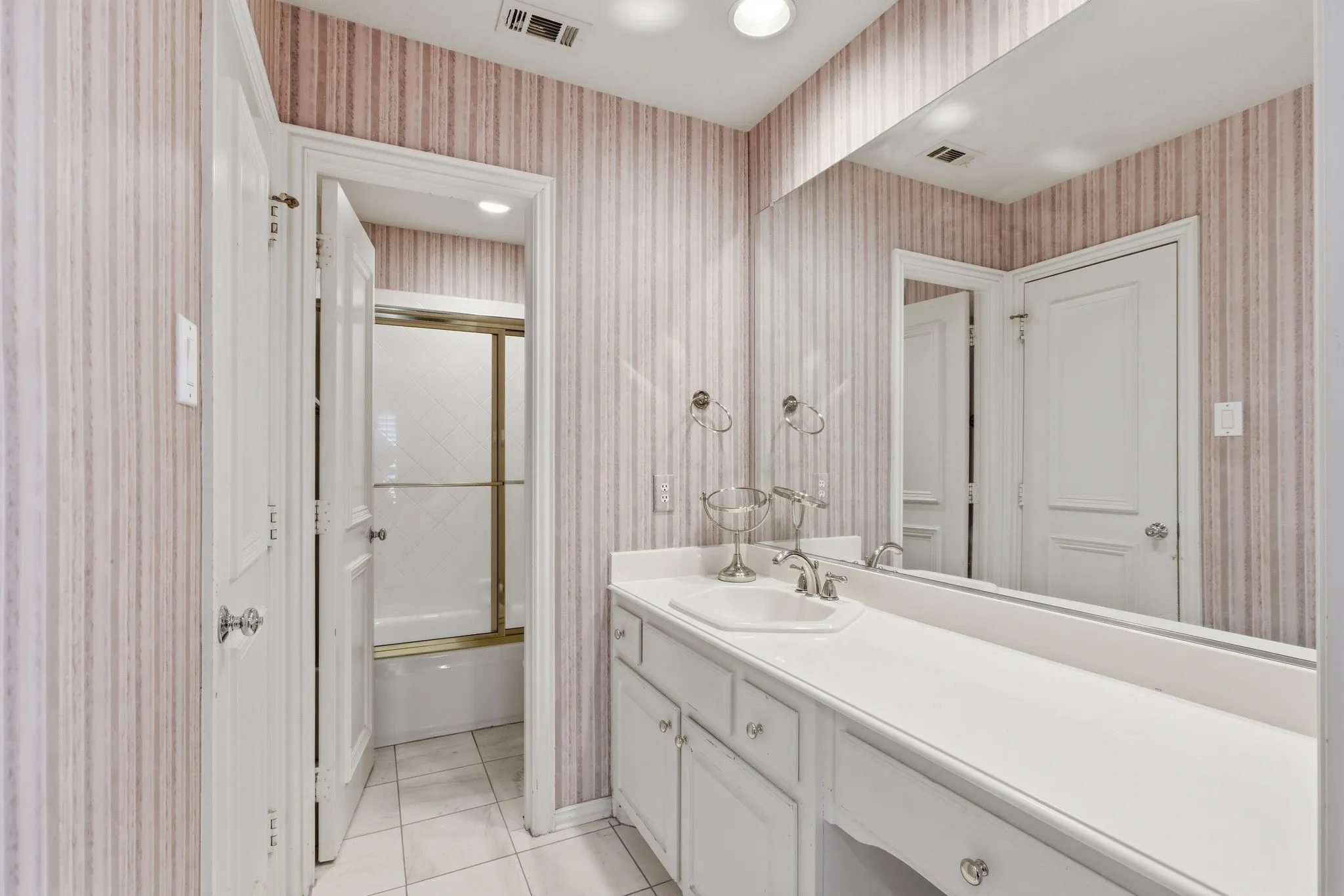 Bathroom featuring vanity, enclosed tub / shower combo, light tile patterned floors, and wallpapered walls