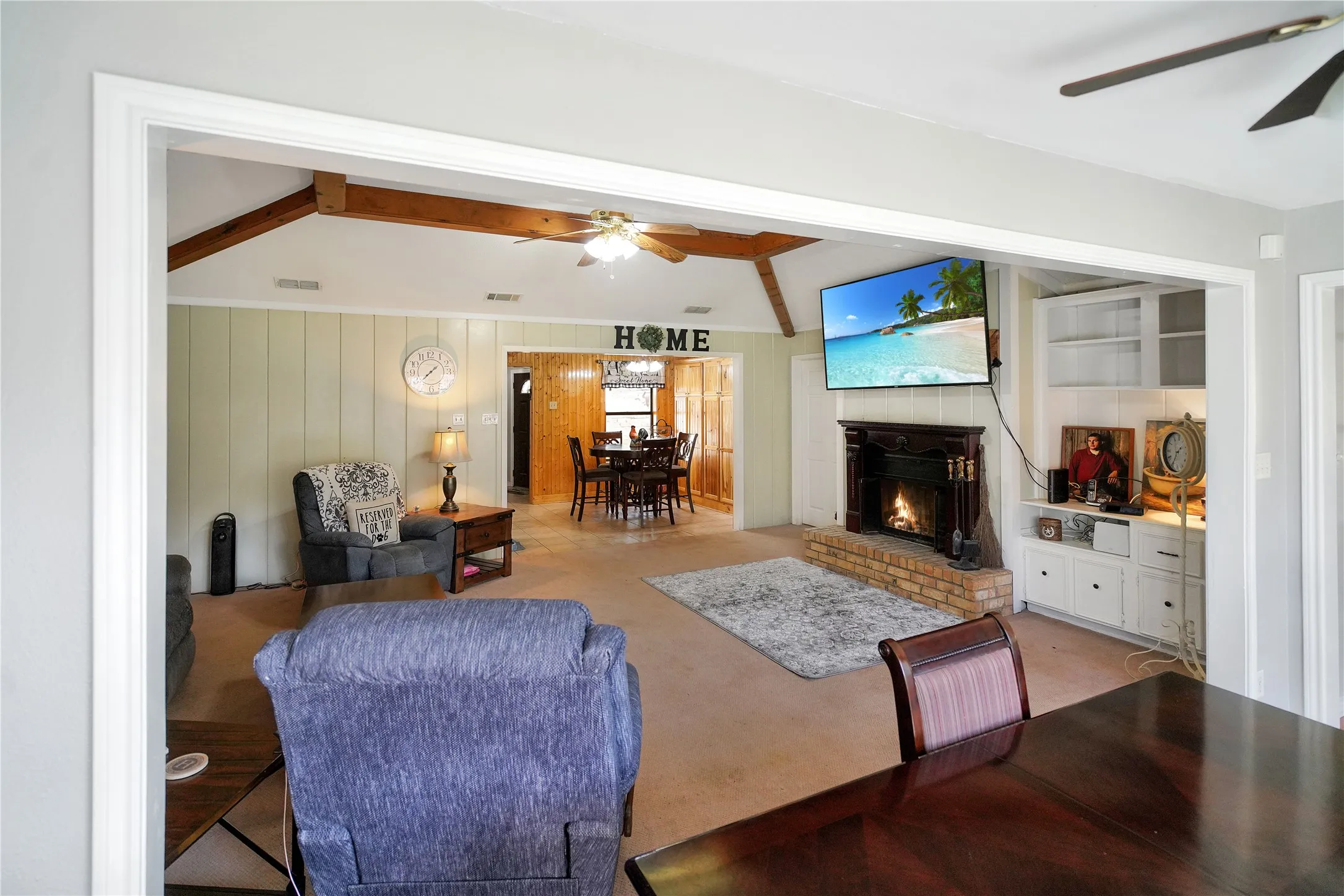 Living area featuring ceiling fan, a fireplace, carpet floors, and beamed ceiling