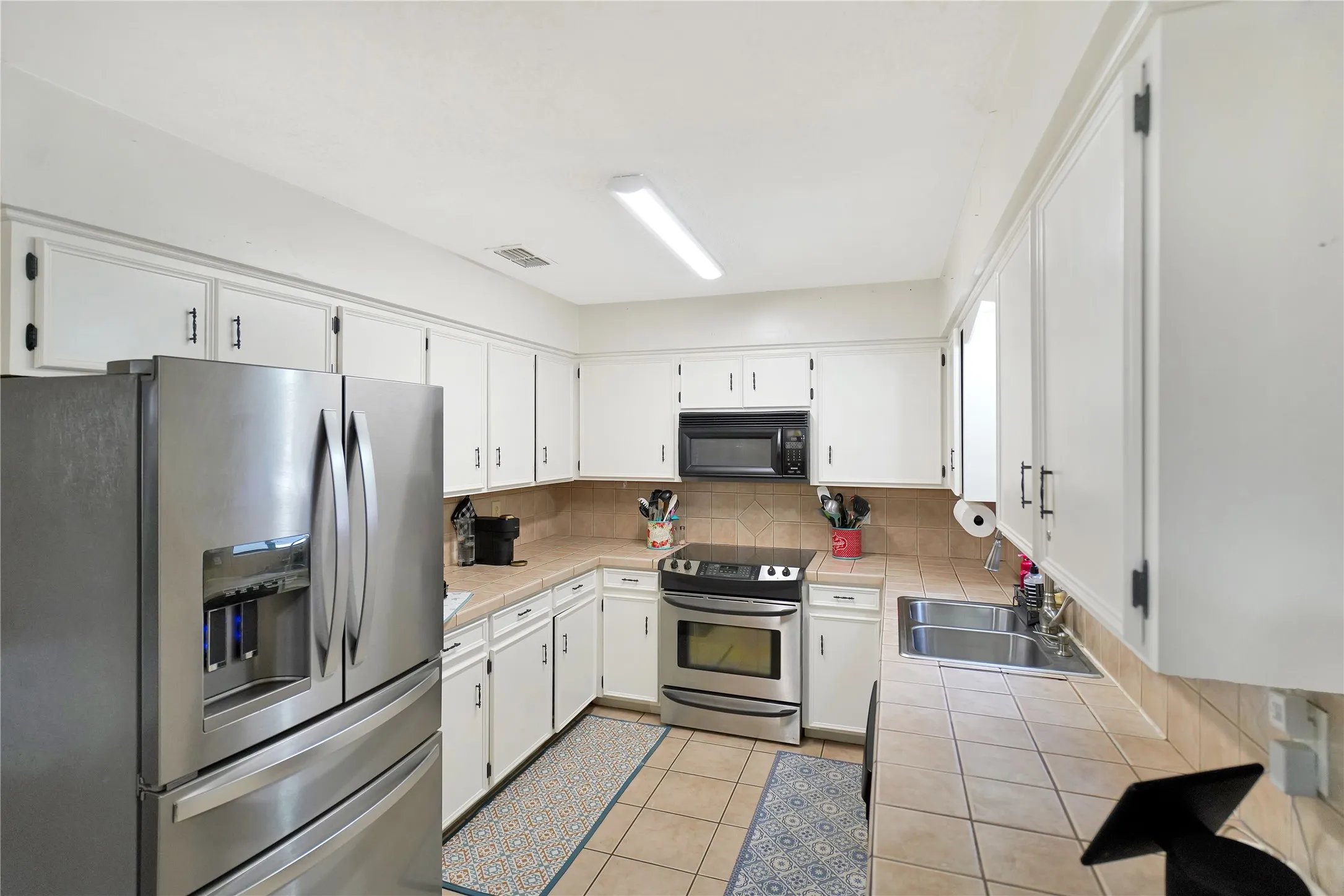 Kitchen featuring tile countertops, appliances with stainless steel finishes, white cabinetry, light tile patterned floors, and tasteful backsplash