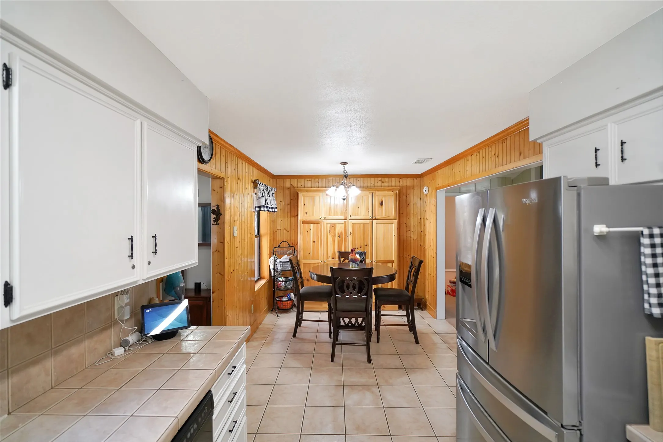 Kitchen featuring tile countertops, stainless steel refrigerator with ice dispenser, white cabinetry, decorative light fixtures, and crown molding