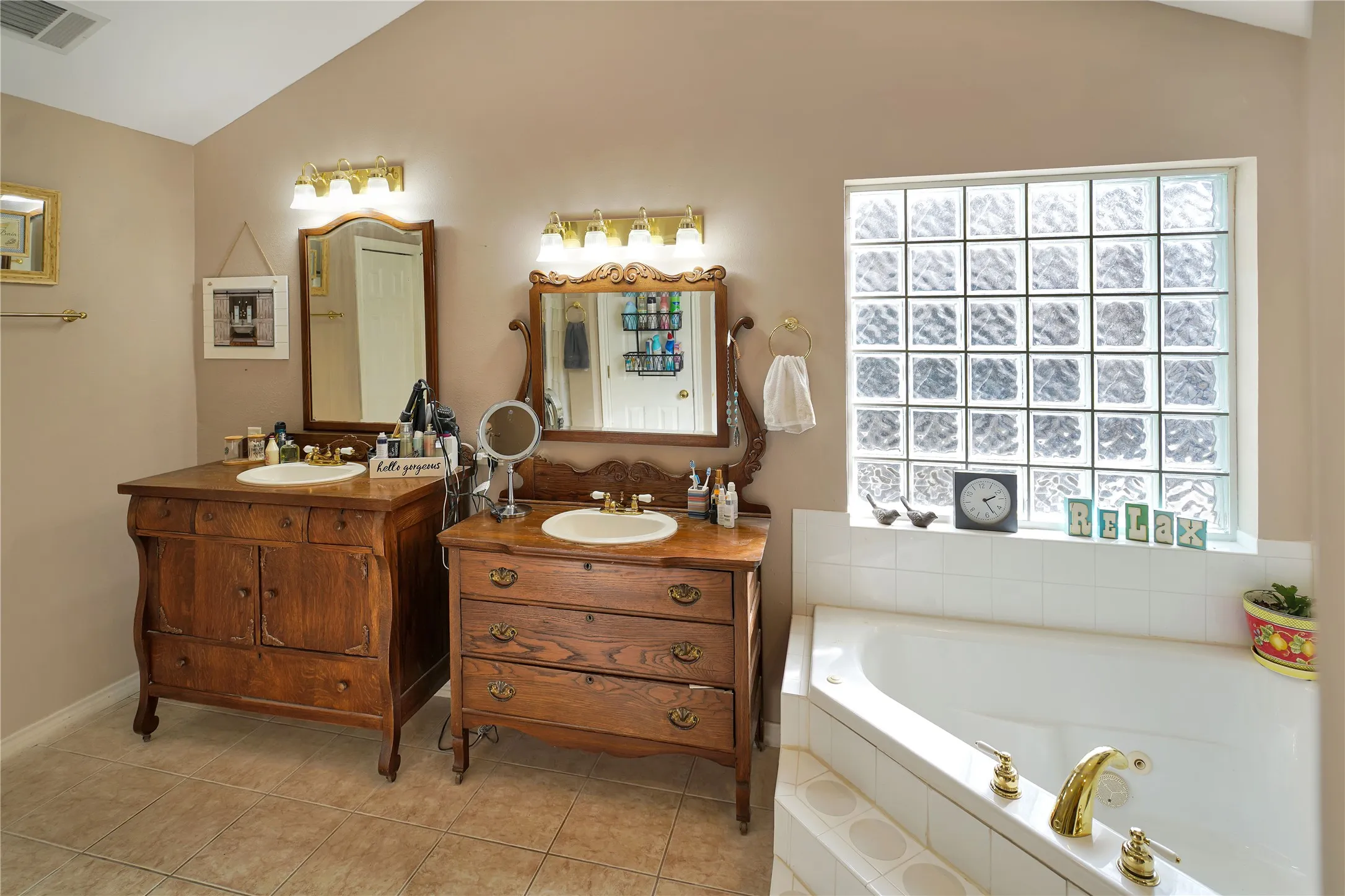 Full bath featuring lofted ceiling, two vanities, a jetted tub, and light tile patterned floors