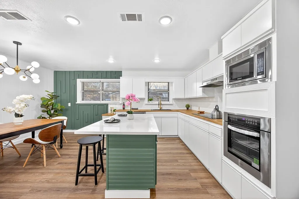 Kitchen featuring white cabinetry, green cabinets, a kitchen breakfast bar, appliances with stainless steel finishes, and a kitchen island