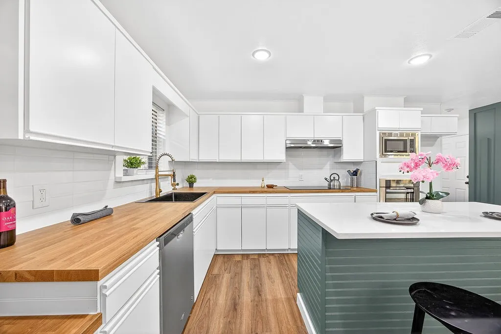 Kitchen featuring light countertops, white cabinets, stainless steel appliances, decorative backsplash, and light wood-style floors