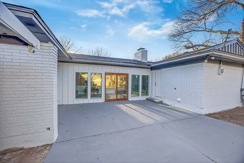 Back of house featuring brick siding, a chimney, a patio, and board and batten siding