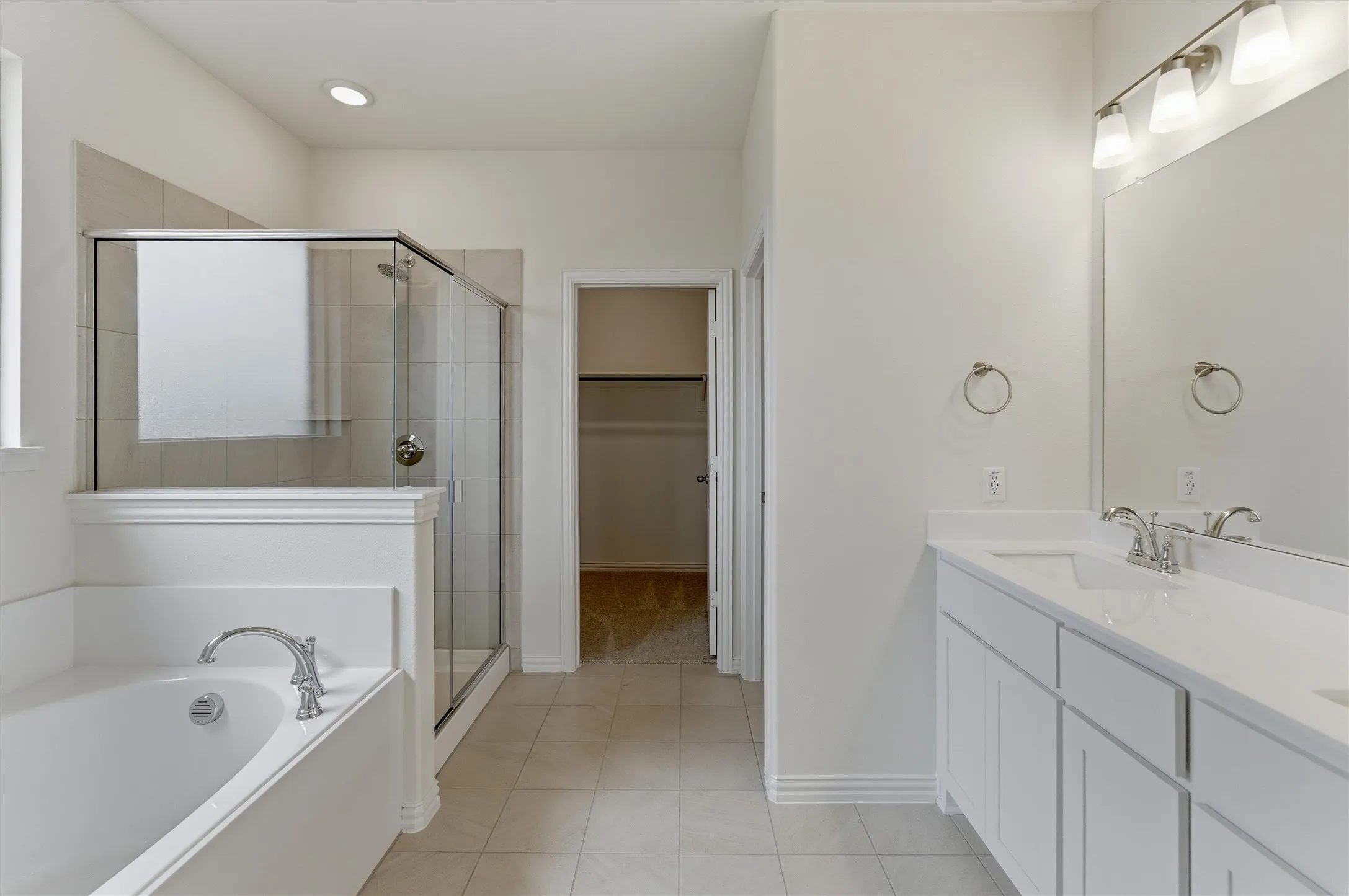 Bathroom featuring a dual vanity with white cabinetry and integrated sinks, a separate walk-in shower with glass enclosure, a built-in soaking tub, and tile flooring