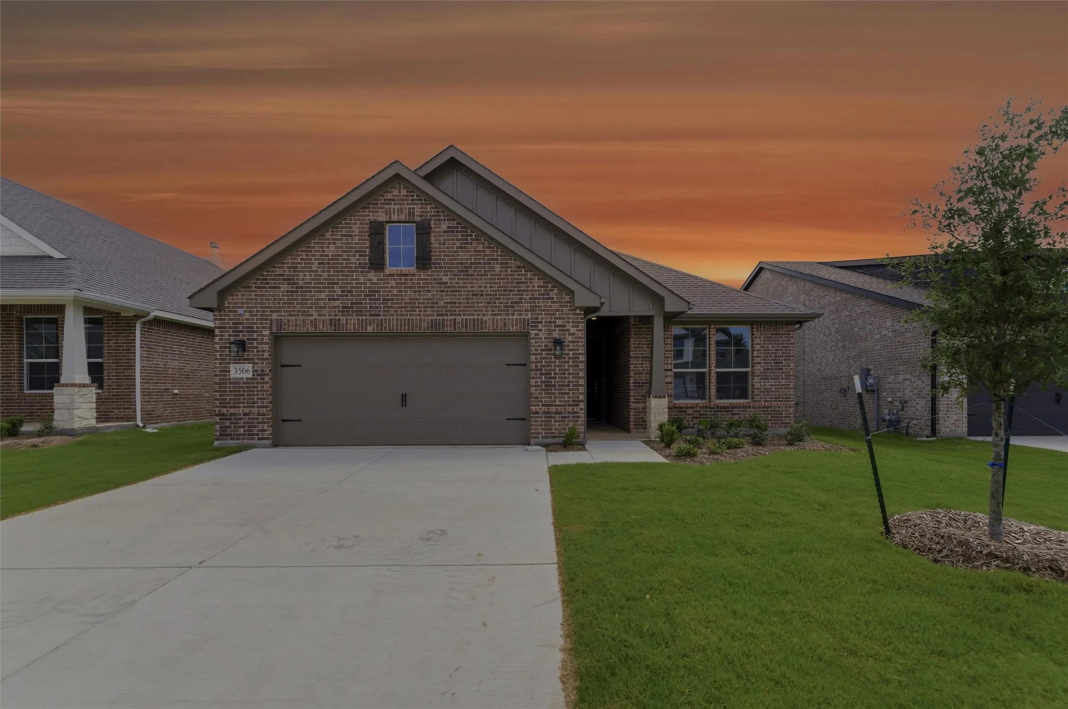 Brick exterior featuring a gabled roofline, an attached garage with decorative hardware, a concrete driveway, and established landscaping