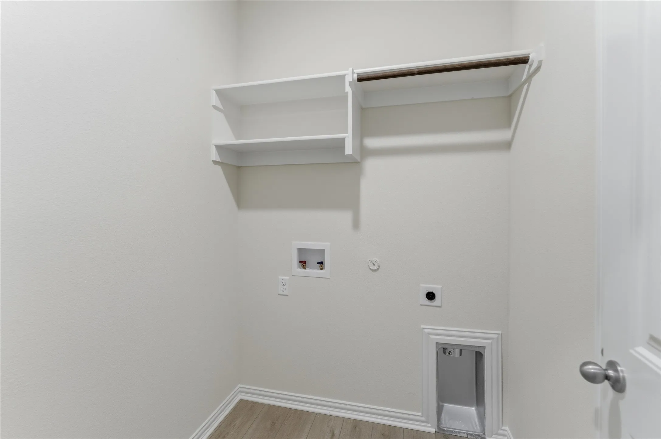 Dedicated laundry area featuring a light wood-finish floor, white baseboards, and built-in white shelving