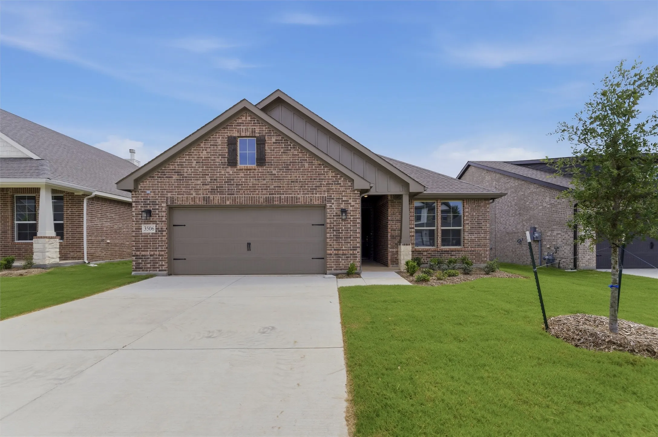Brick facade residence featuring an attached garage, a paved driveway, and established landscaping