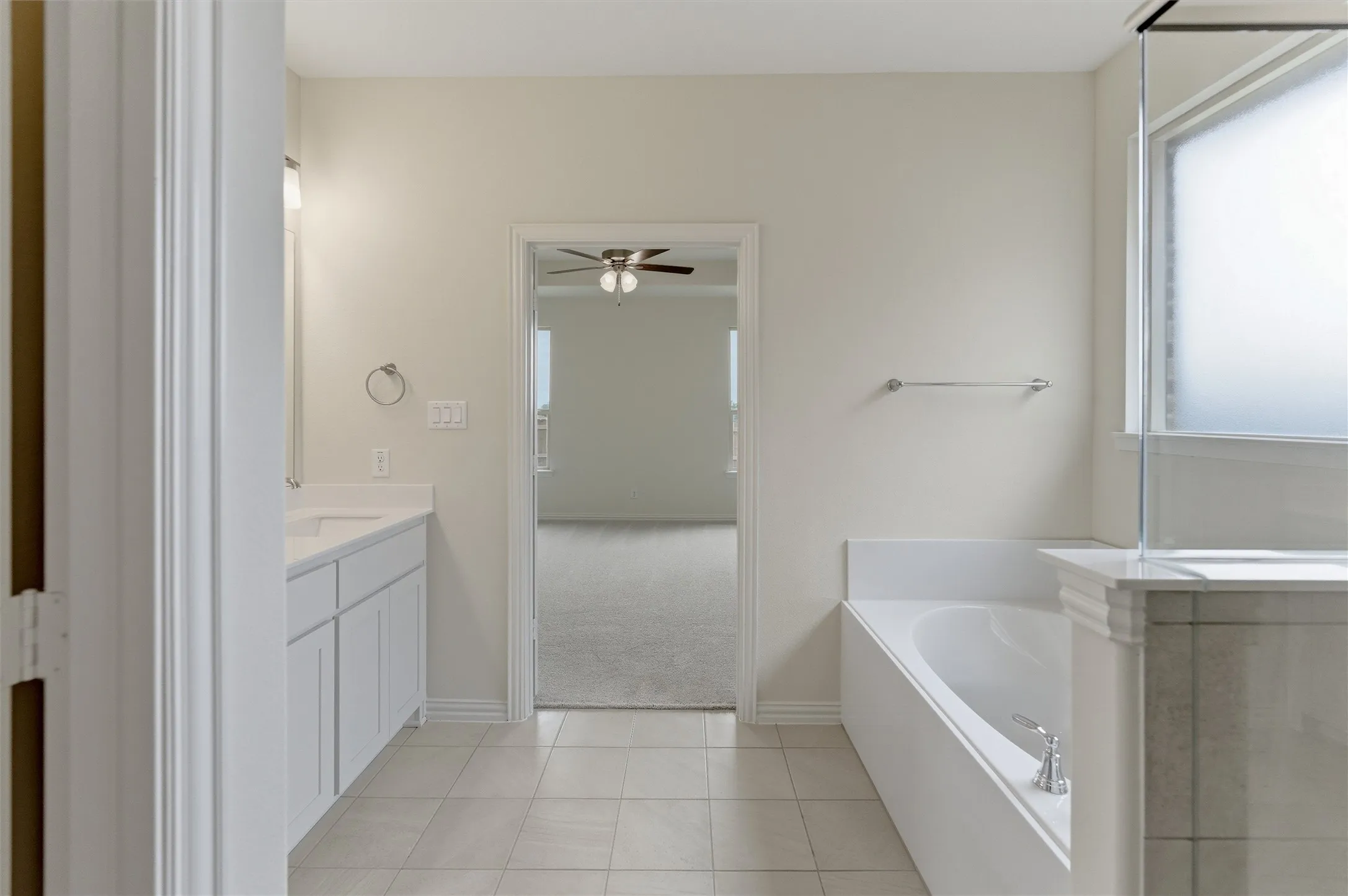 Bathroom featuring a white dual vanity with undermount sinks, a built-in soaking tub, a tiled shower with glass enclosure, and light tile flooring
