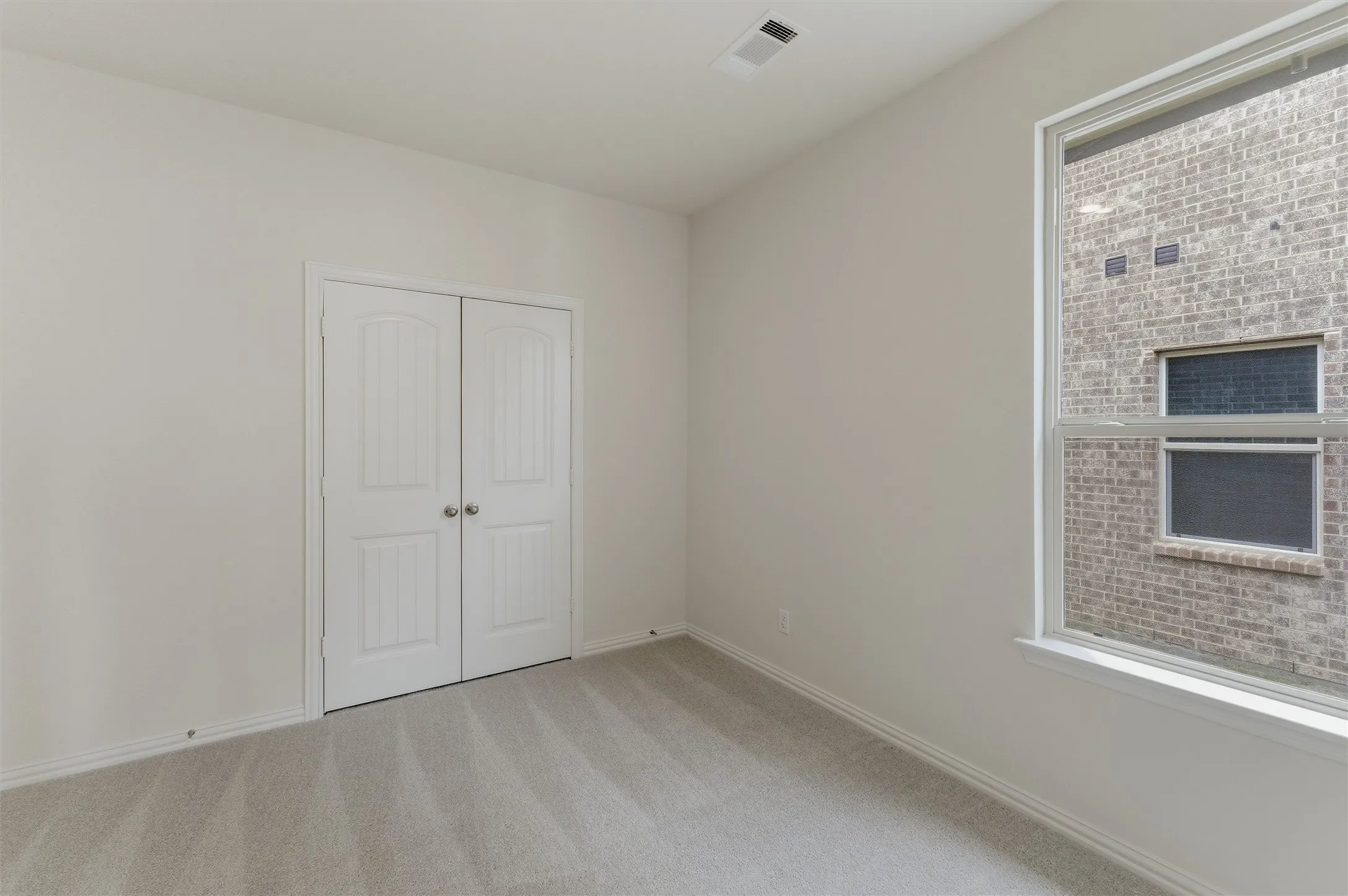 Neutral wall paint, light-toned carpeting, and a large window providing natural light
