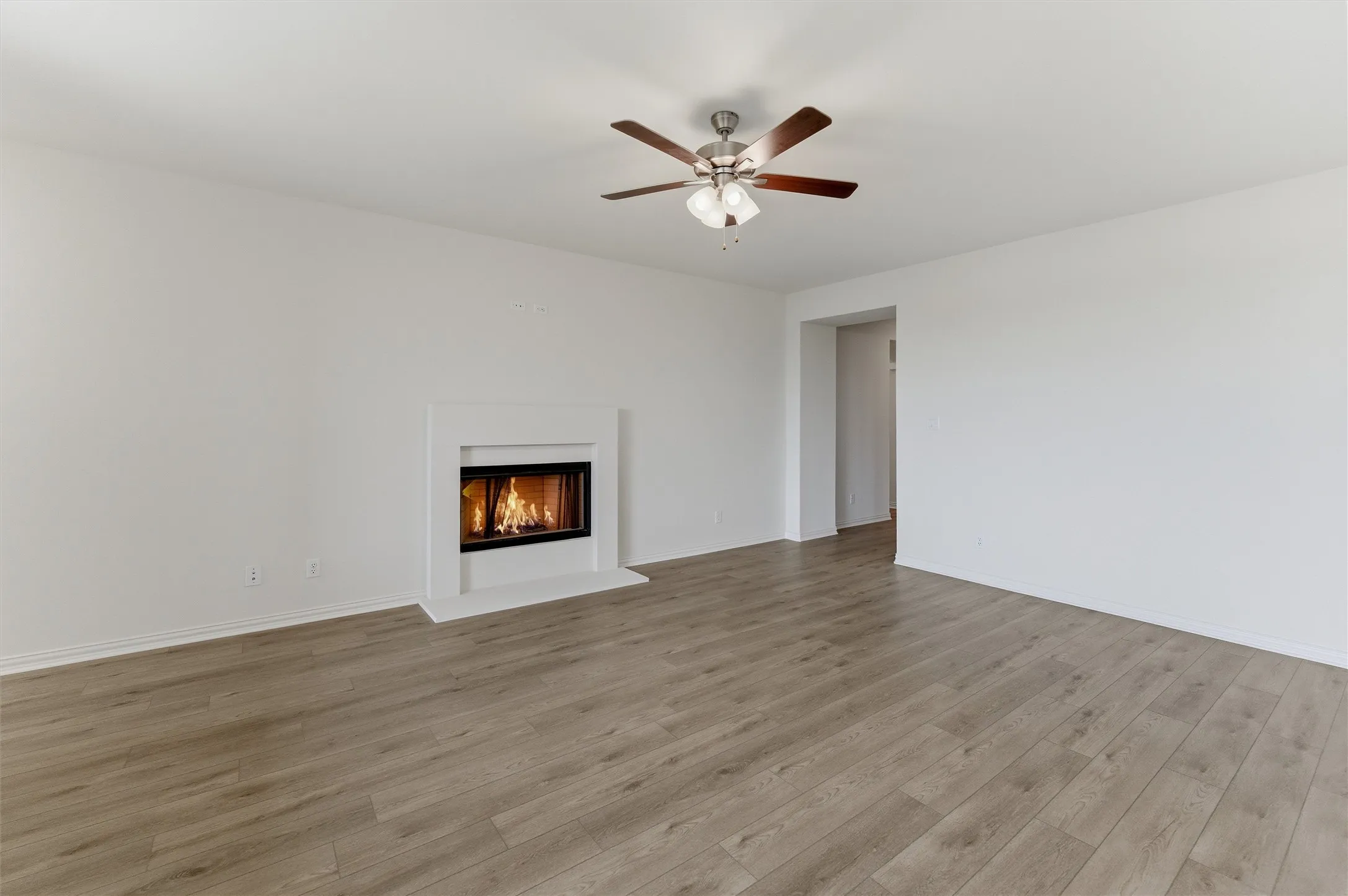 Living space featuring a built-in fireplace with a white mantel, wood-finish flooring, a ceiling fan, and white walls