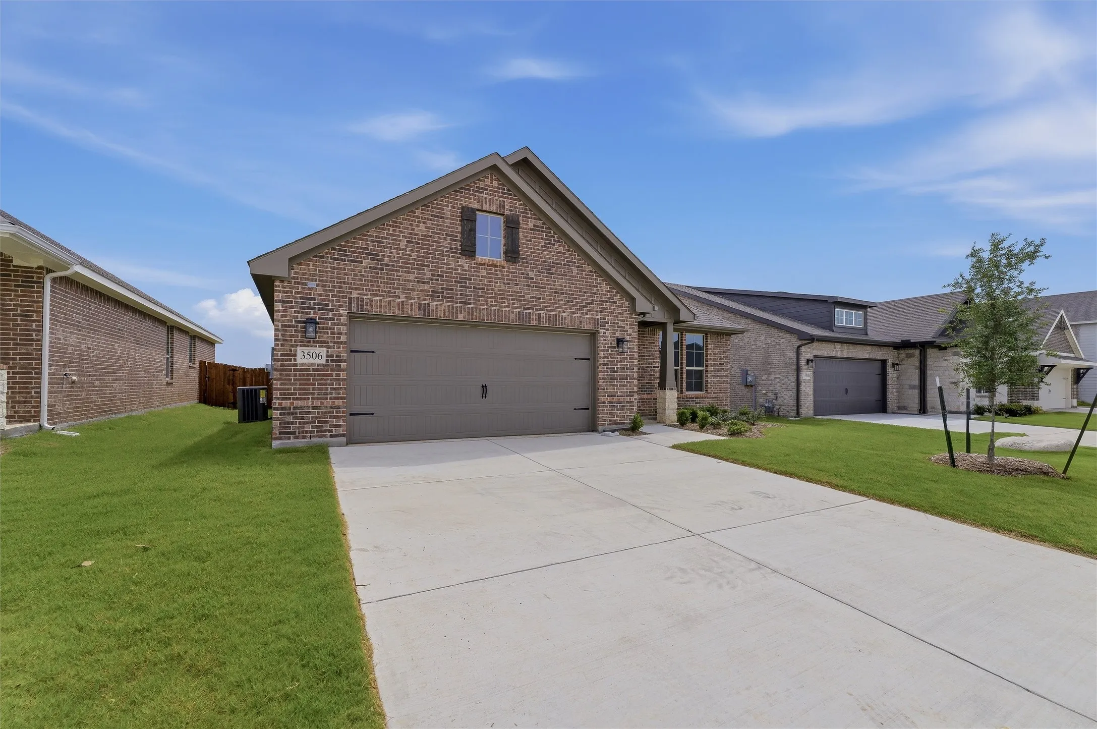 Brick exterior with a gabled roofline, featuring a two-car garage with decorative hardware, a concrete driveway, and established landscaping