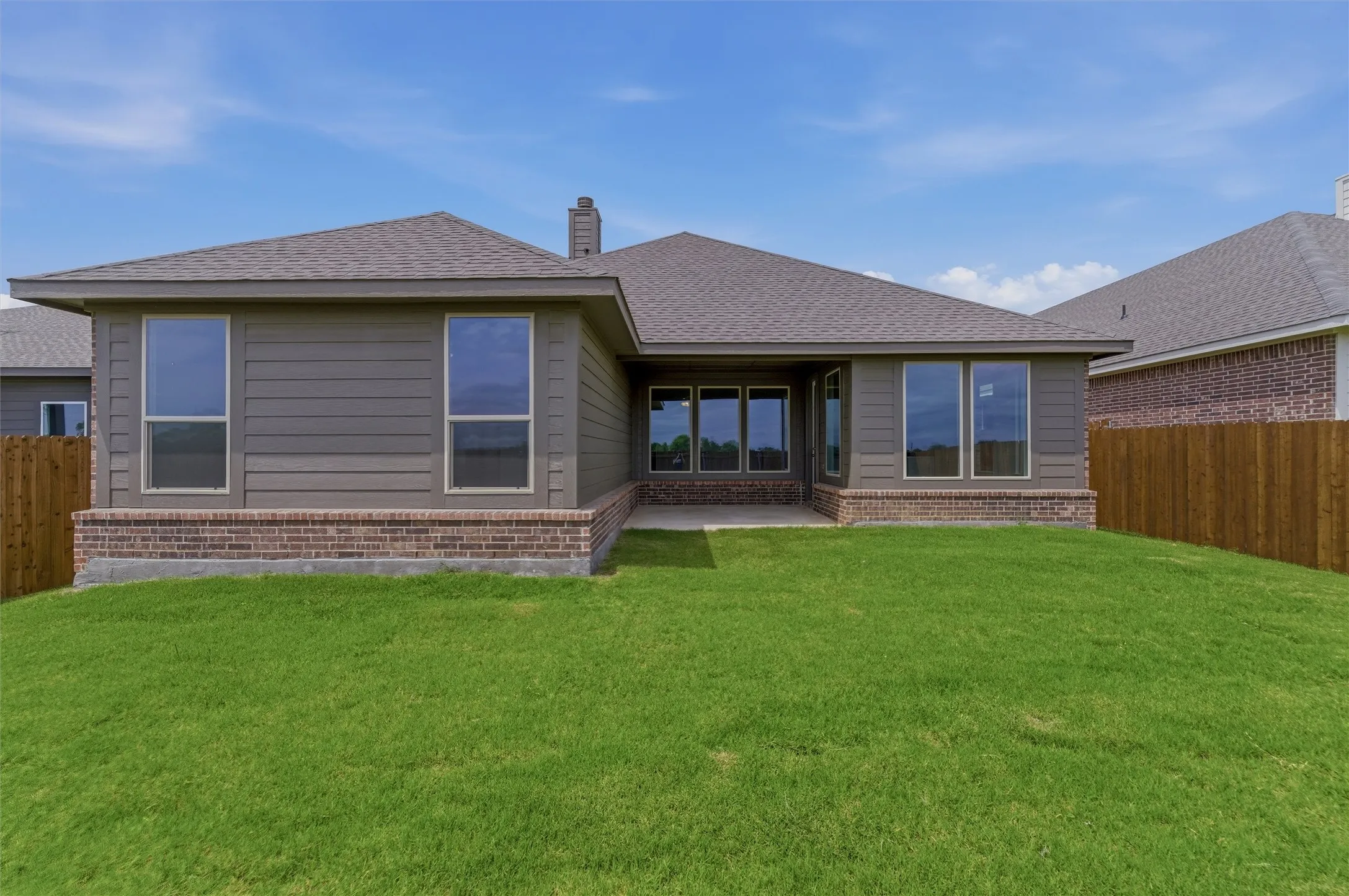 Expansive backyard featuring a lush green lawn, full privacy fencing, and a concrete patio