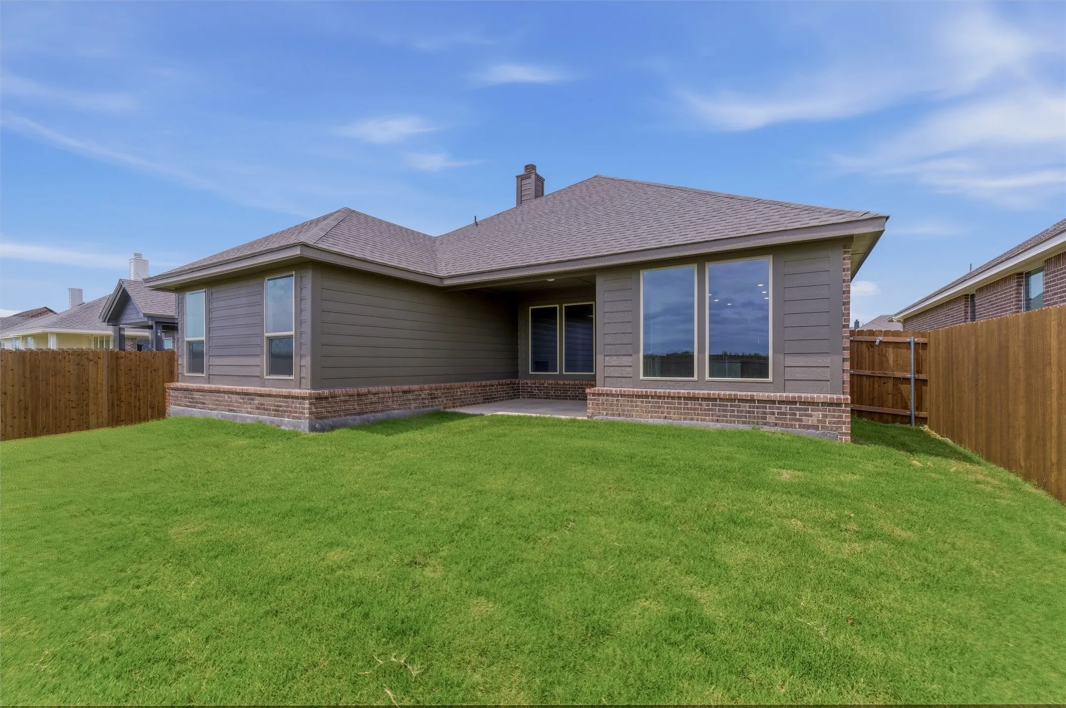 Expansive backyard featuring a manicured lawn, wood fencing, and a covered patio area