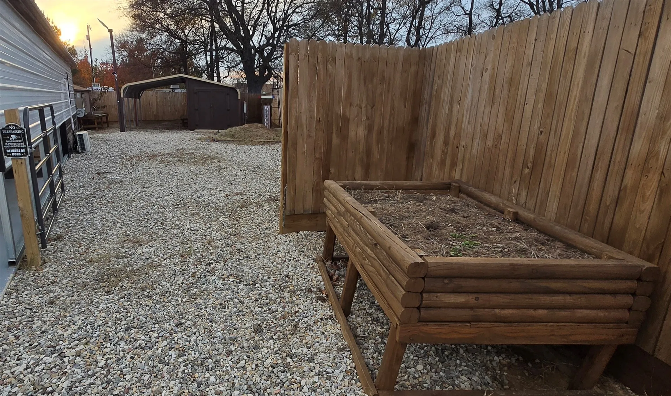 Yard at dusk with a vegetable garden, a carport, and an outbuilding