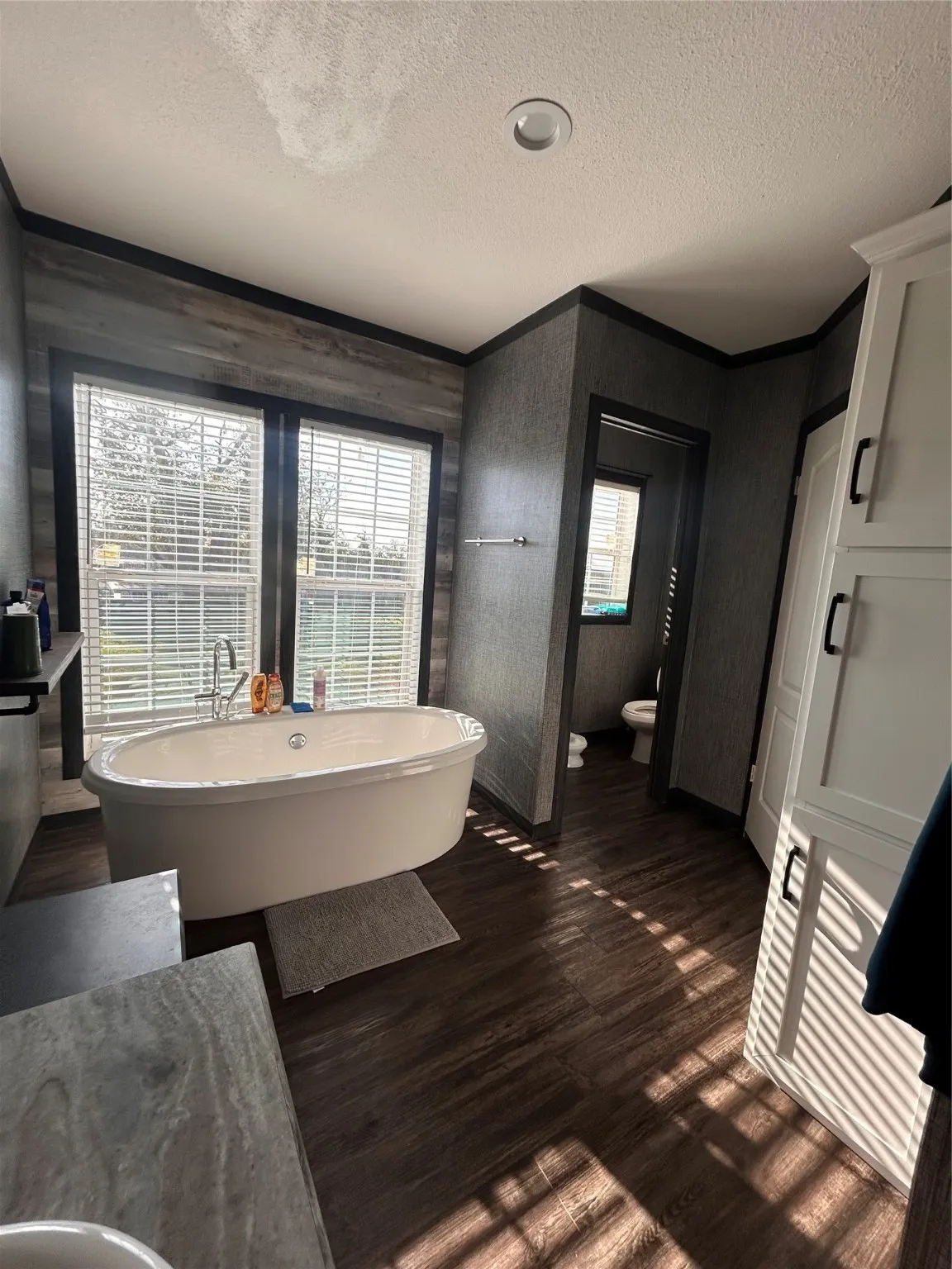 Bathroom featuring a textured ceiling, a freestanding bath, a bidet, dark wood-style flooring, and crown molding