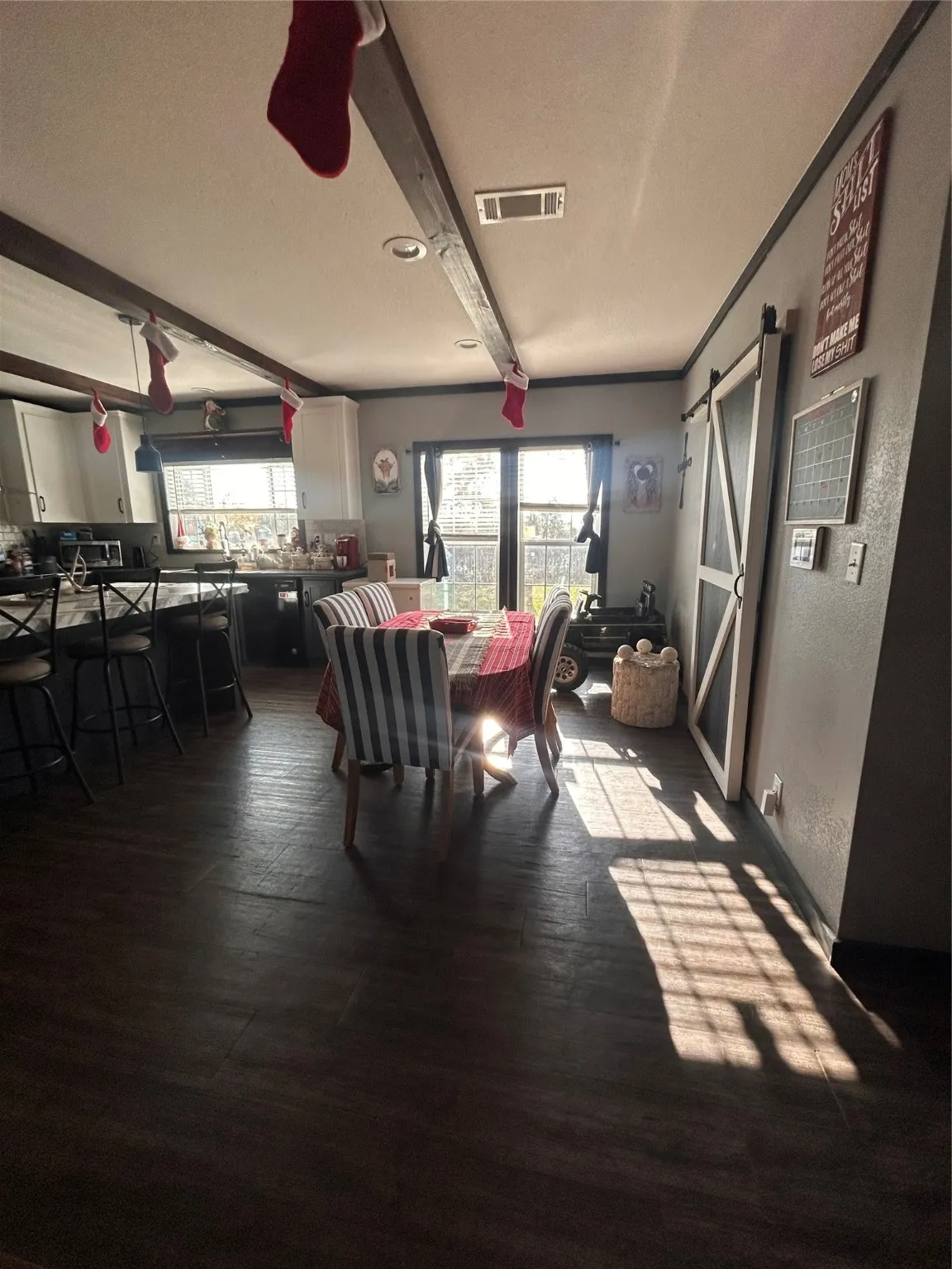 Dining room with a barn door, beam ceiling, and dark wood-style floors