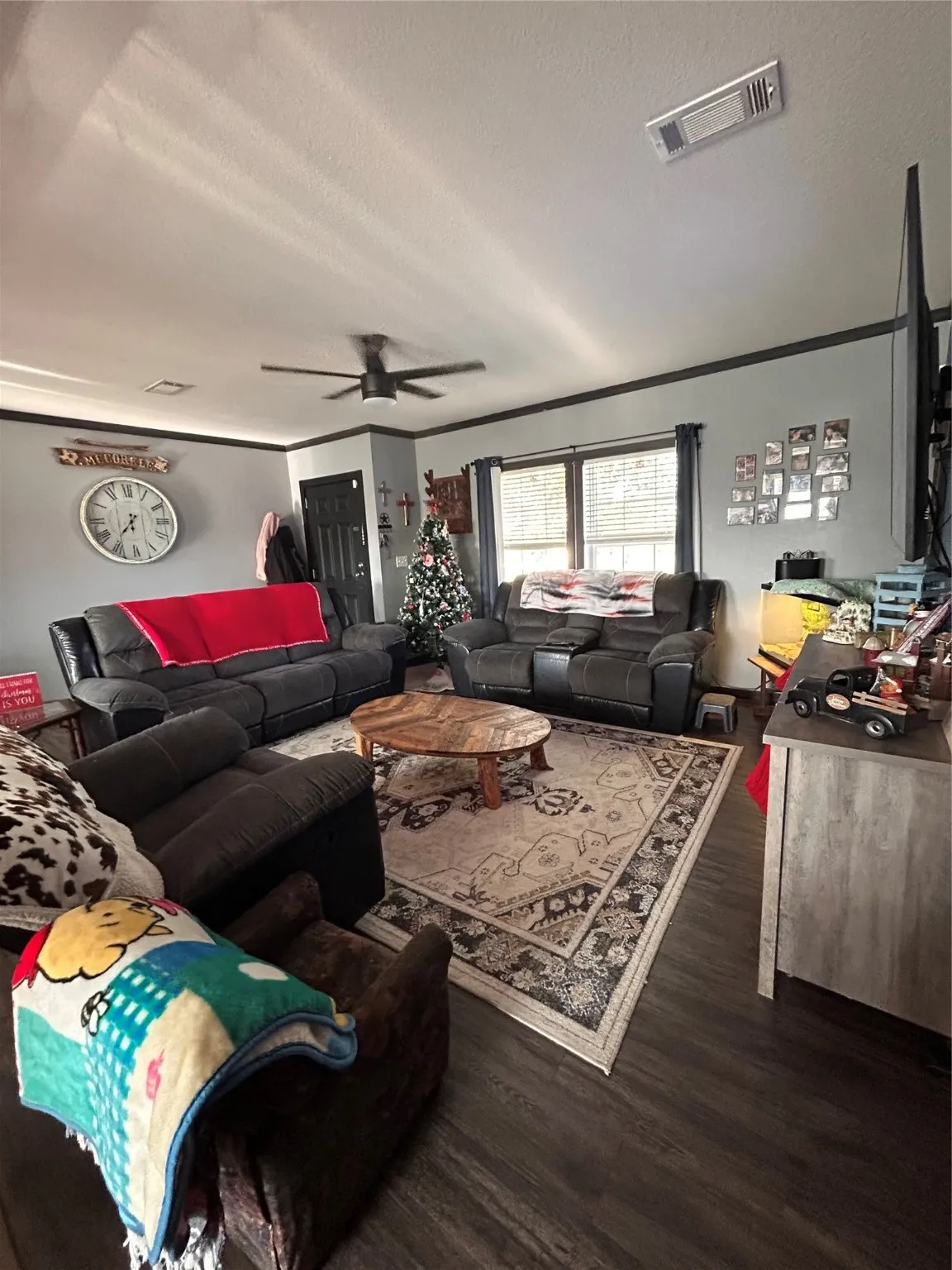 Living room with a ceiling fan, wood finished floors, ornamental molding, and a textured ceiling