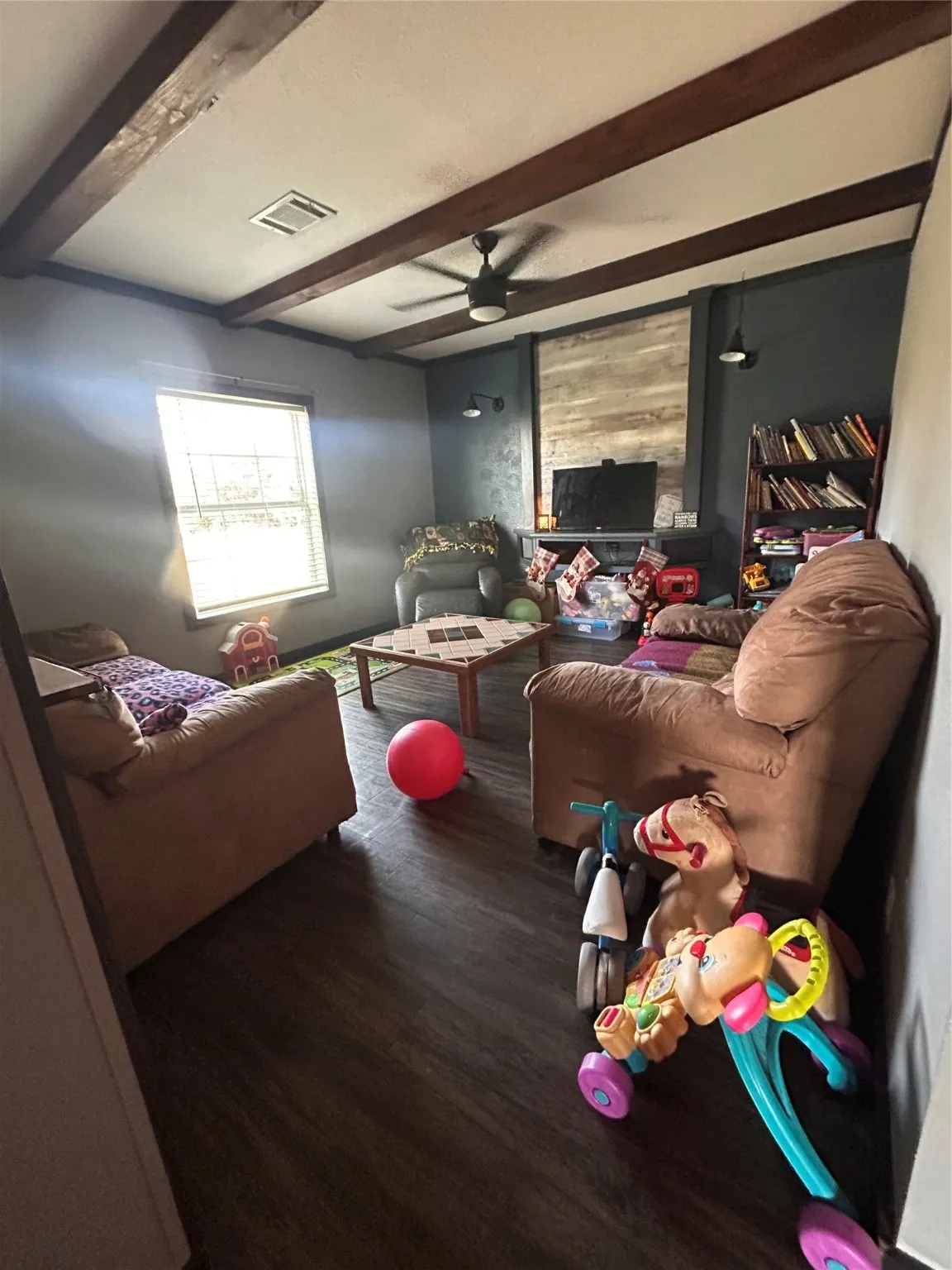 Living area featuring beamed ceiling, wood finished floors, and ceiling fan
