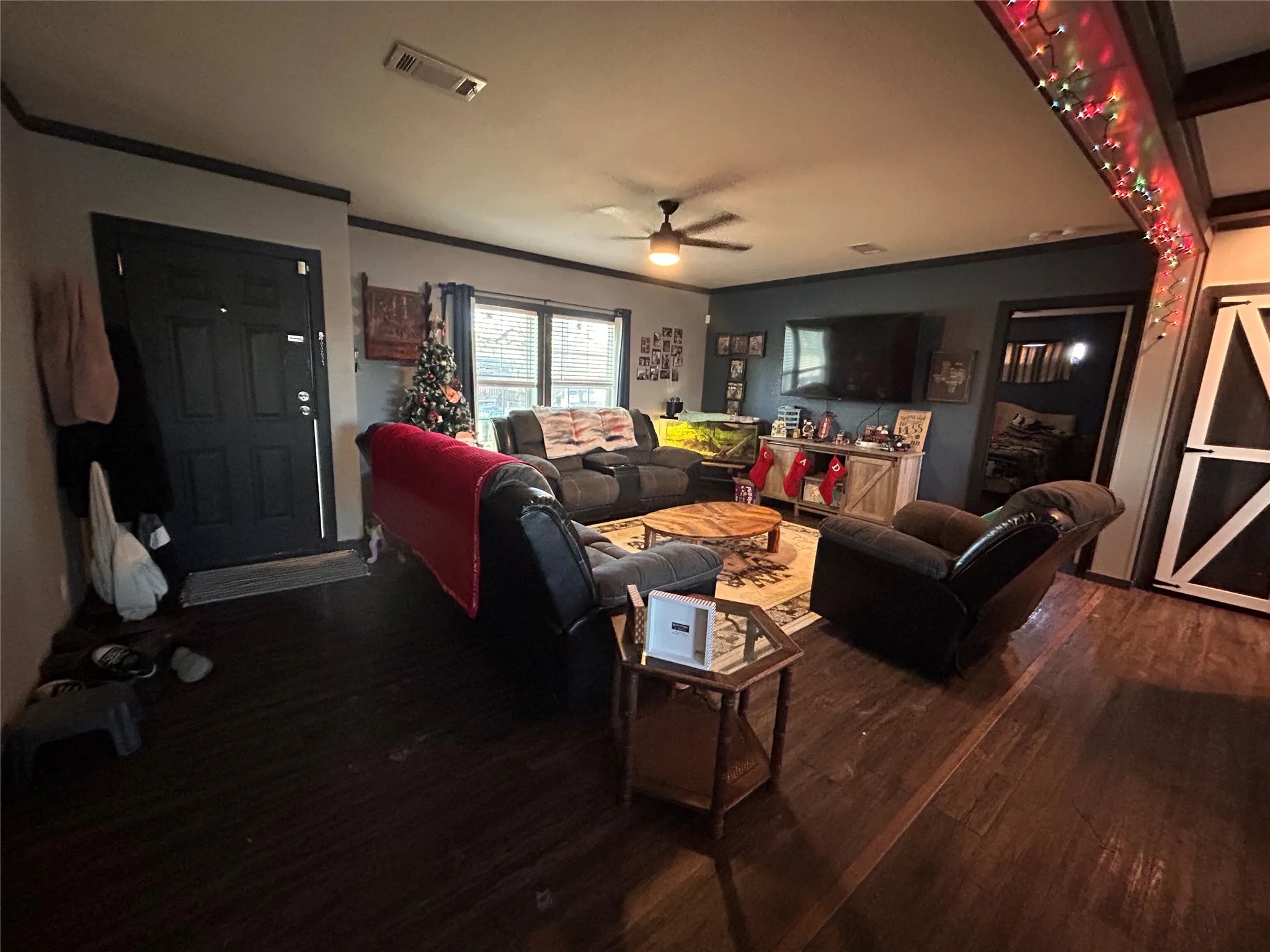 Living area featuring dark wood-type flooring, ornamental molding, and a ceiling fan