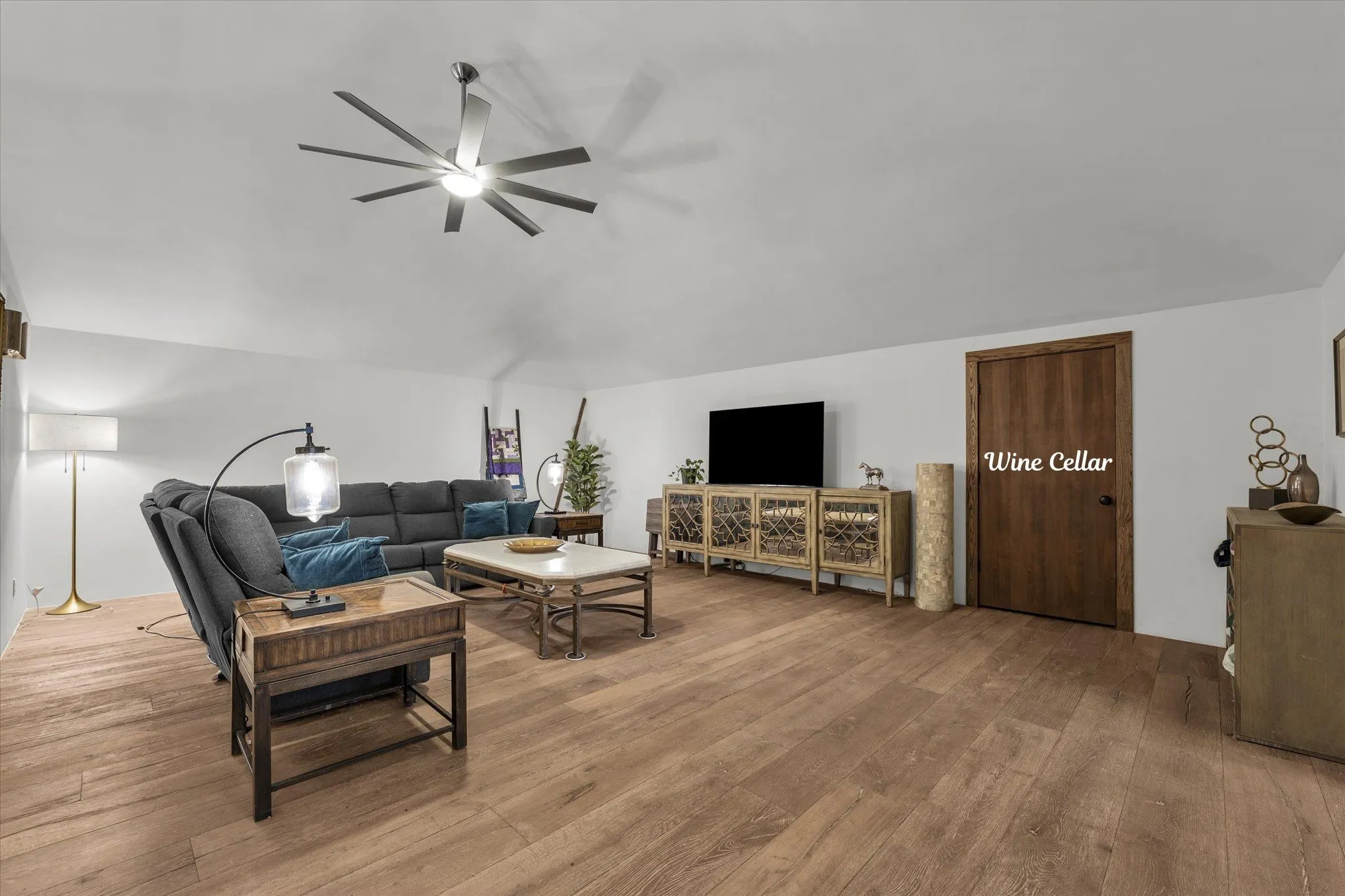 Living area with wood flooring, ceiling fan and safe room that can be used as a wine cellar