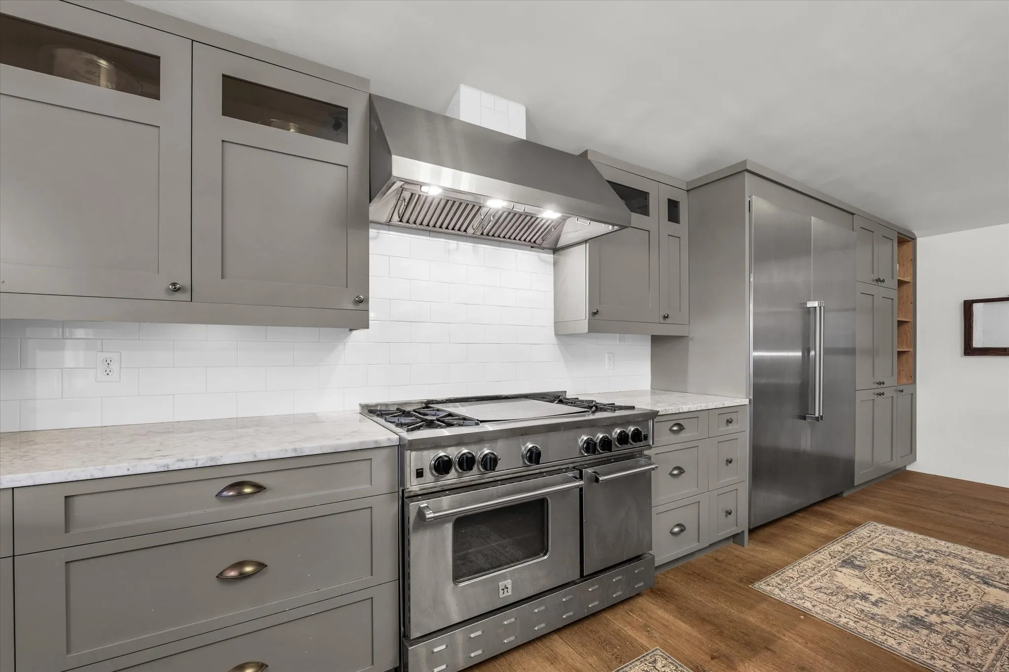 Kitchen with gray cabinets, high end appliances, wall chimney range hood, and wood finished floors