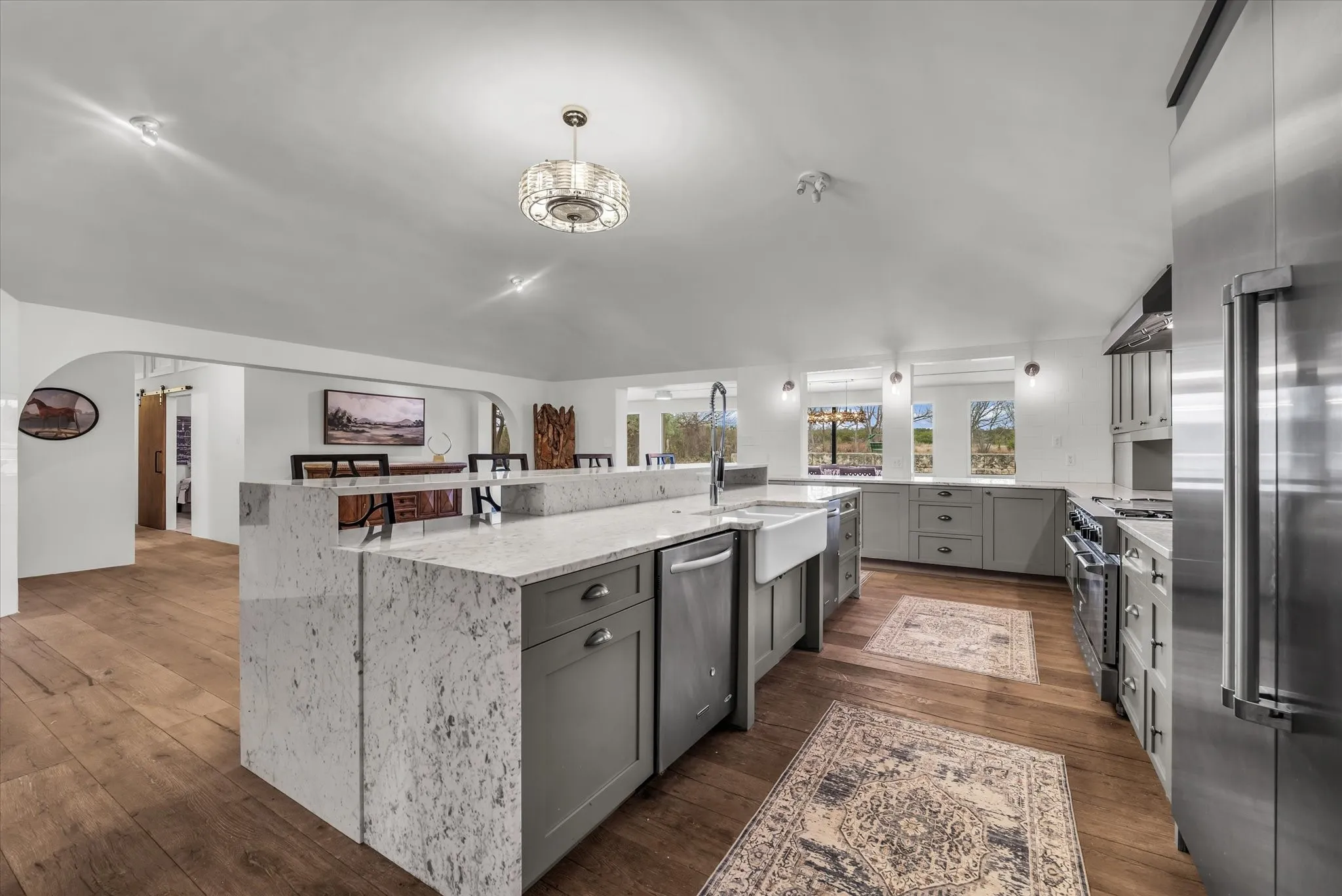 Kitchen with gray cabinetry, high quality appliances, light stone countertops, wood finished floors, and range hood
